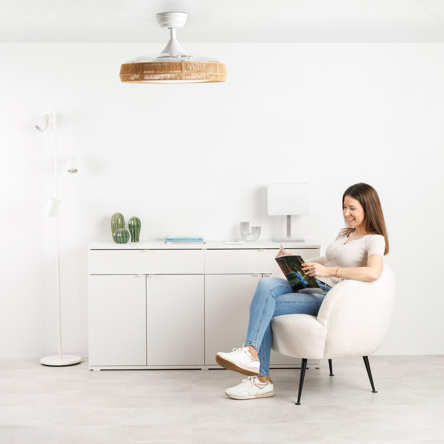 Una mujer sentada en un sillón leyendo una revista. Se ve un ventilador de techo.