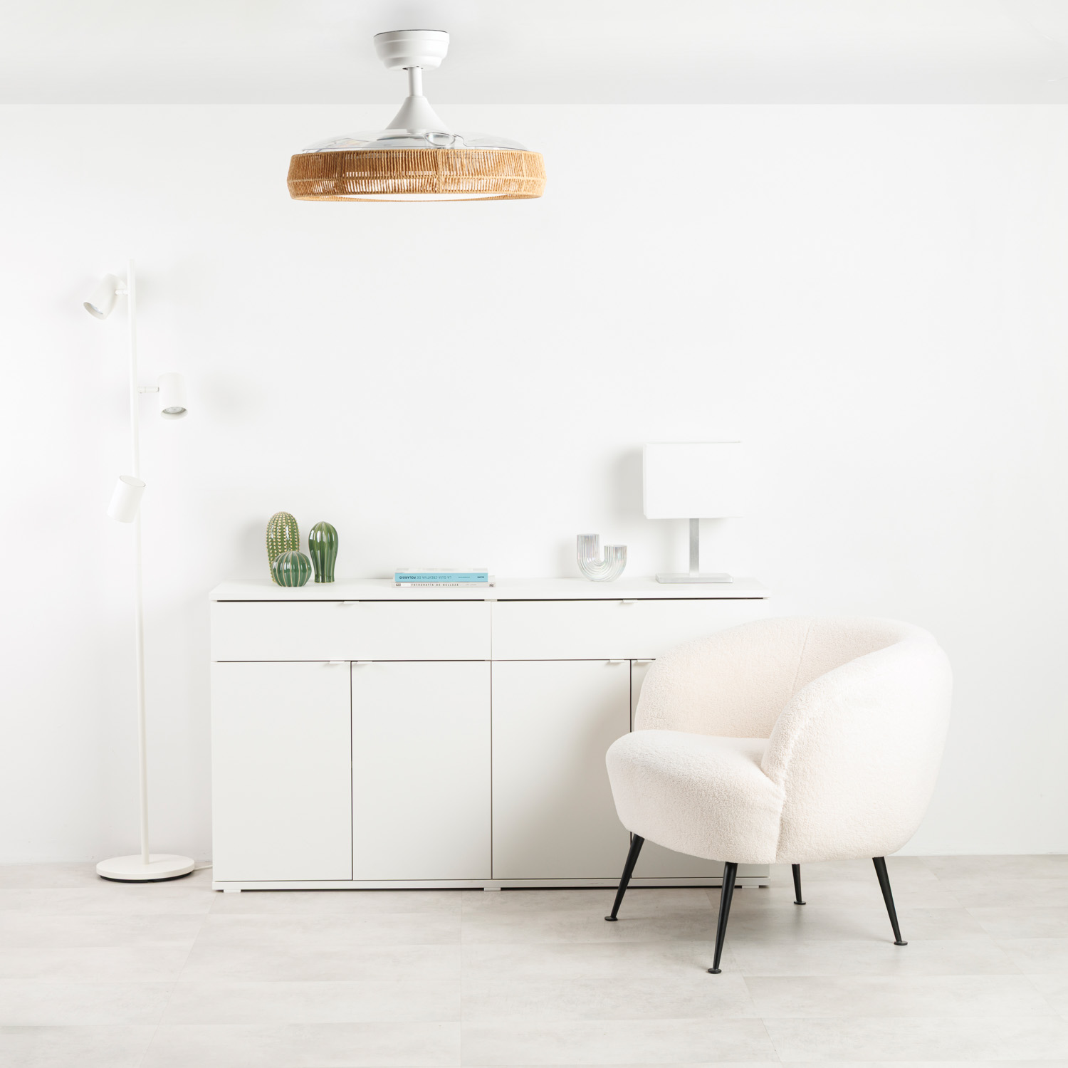 Un sillón blanco junto a un mueble blanco con cactus y libros encima.
