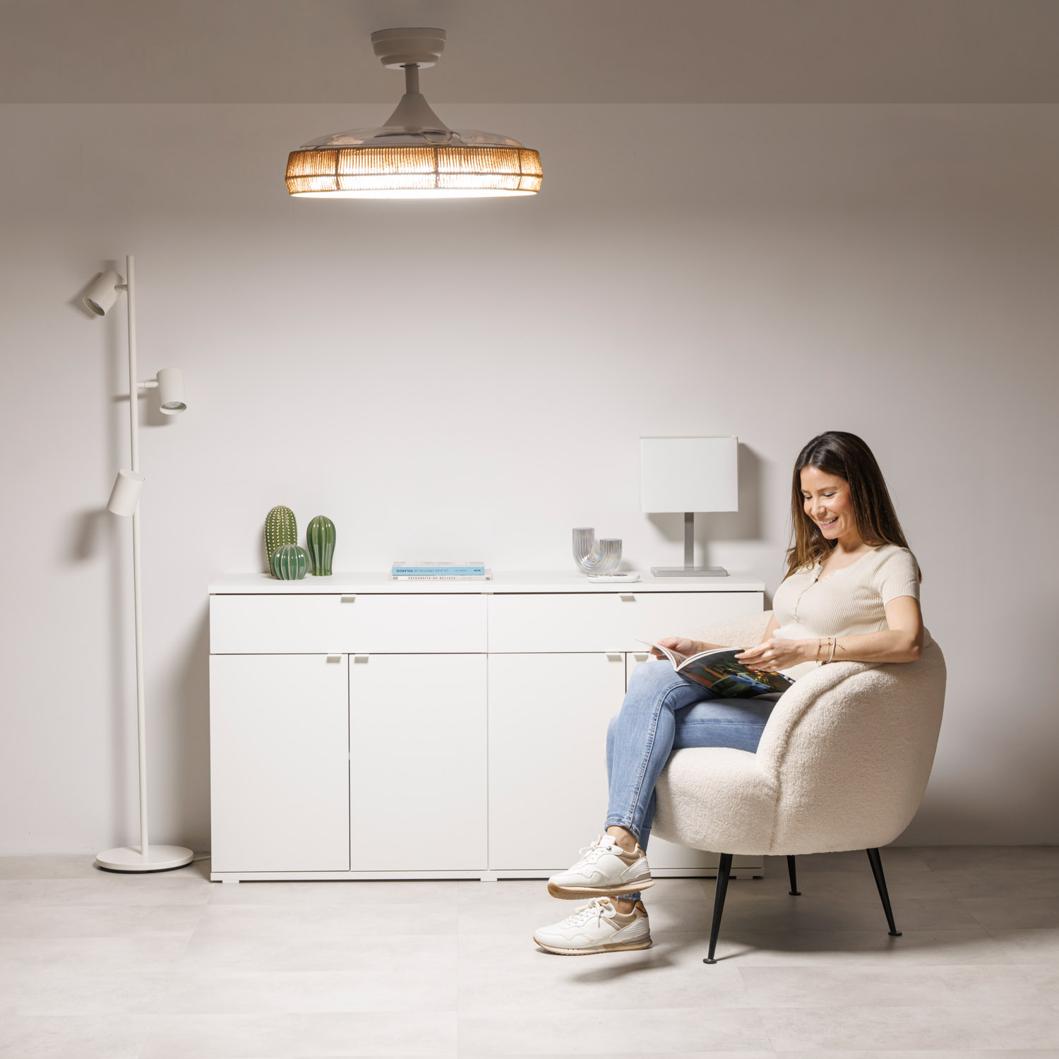 Una mujer lee una revista en un sillón frente a un mueble blanco.