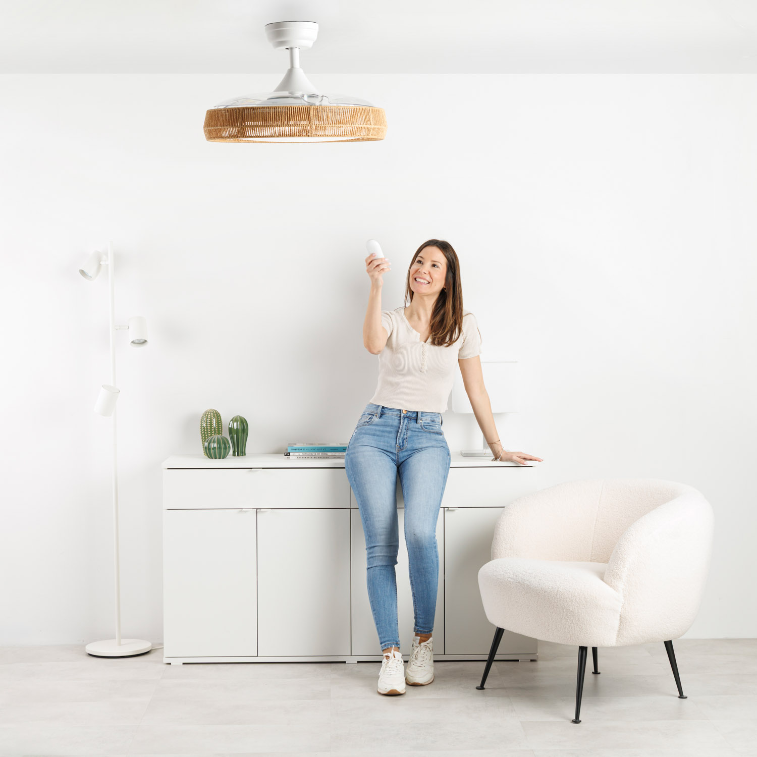 Mujer sostiene control remoto frente a ventilador de techo con detalle de ratán.