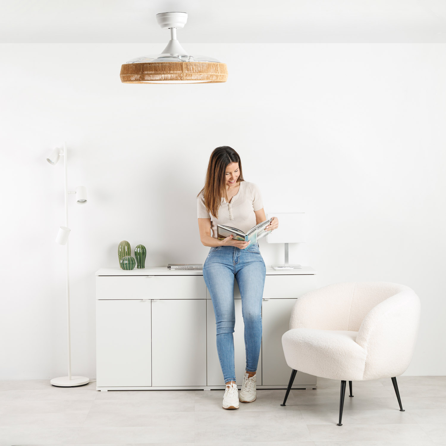 Una mujer lee un libro en una sala luminosa con ventilador de techo y sillón.