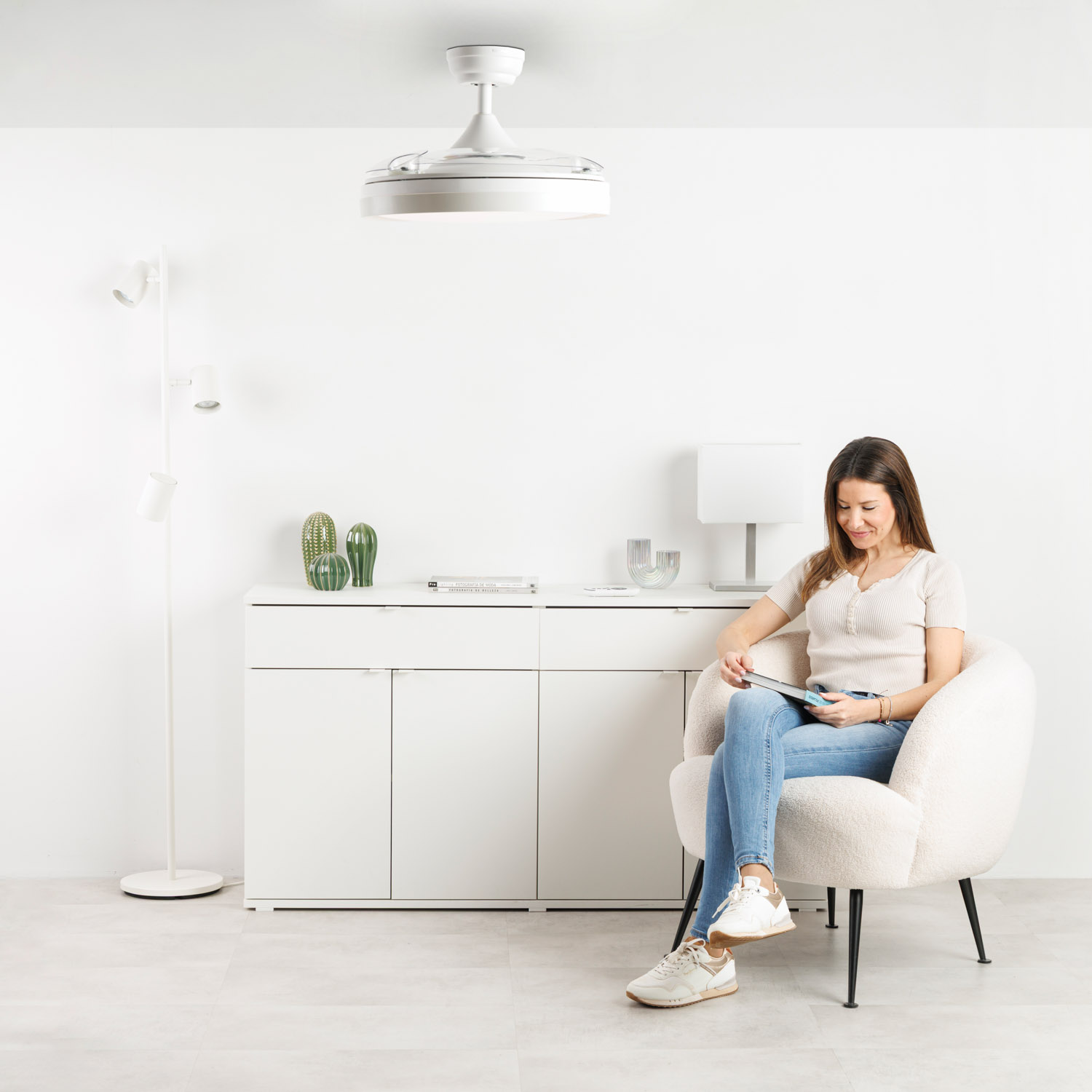 Una mujer se sienta en un sillón blanco, leyendo en una tableta.