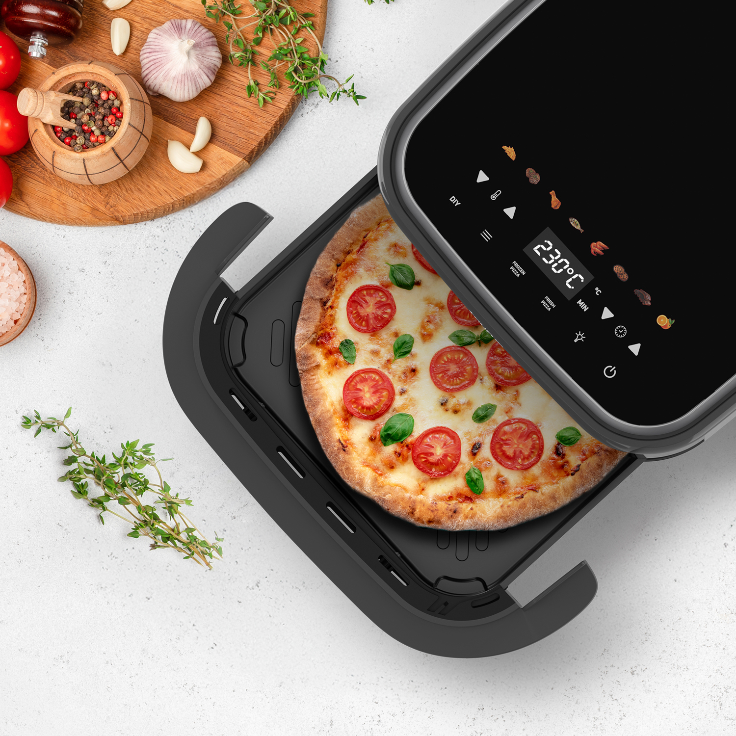 Una pizza con tomates y albahaca en una cesta negra de freidora de aire.