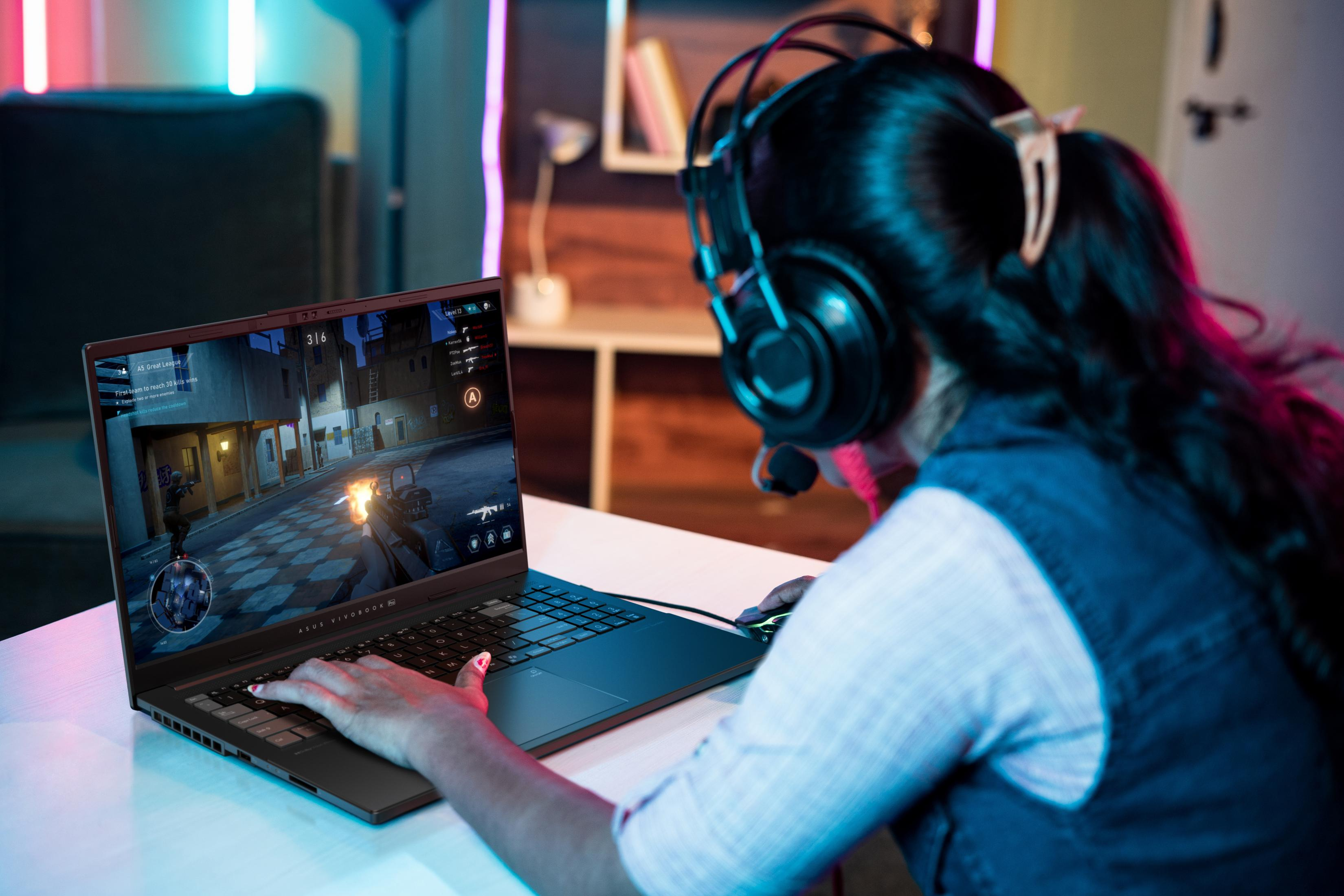 A person plays a first-person shooter game on a laptop wearing headphones.