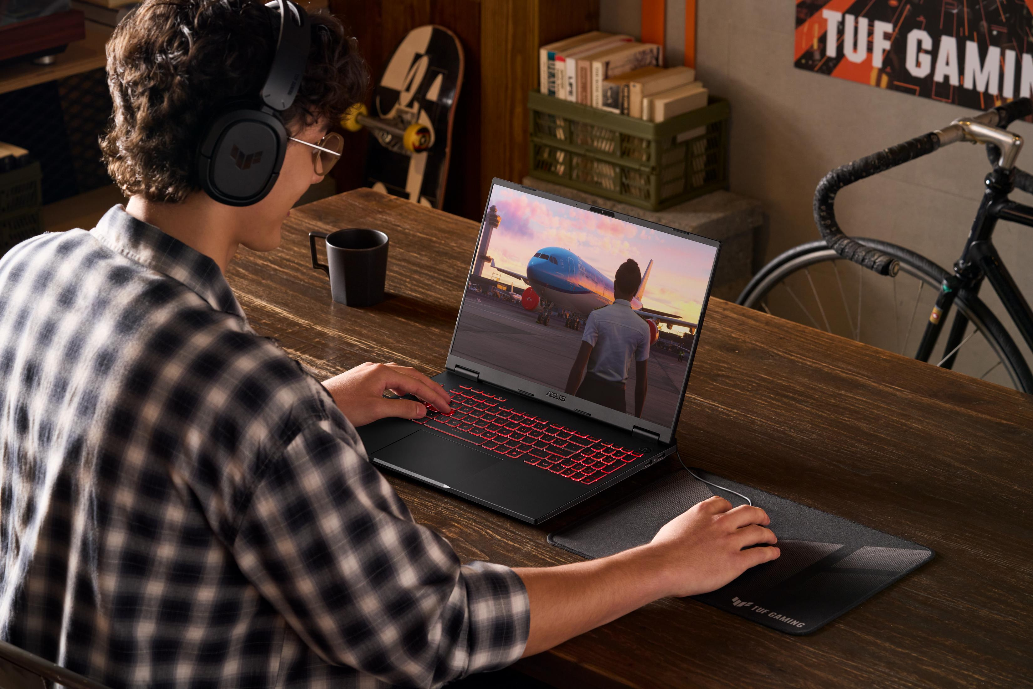 Person wearing headphones plays a flight game on a laptop with a red keyboard.