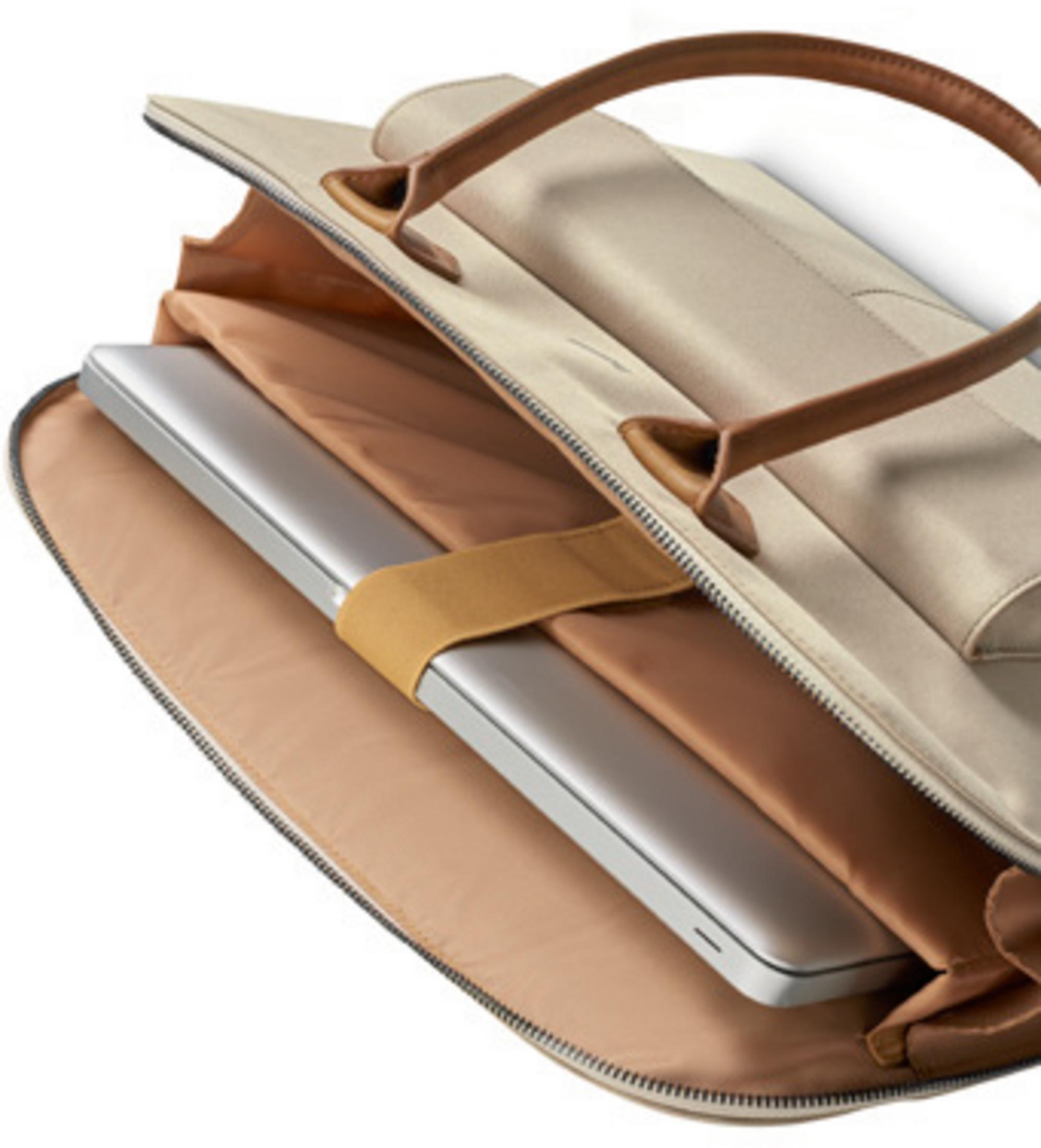 Eine beige Laptoptasche mit braunen Ledergriffen, geöffnet, zeigt einen silbernen Laptop, der mit einem braunen Riemen gesichert ist.