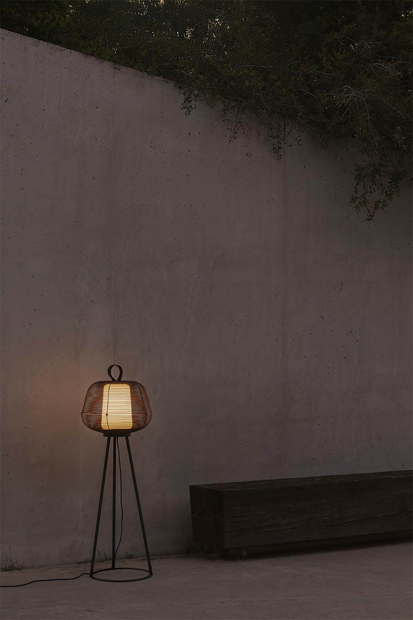 Una lampada da terra con paralume intrecciato illumina uno spazio esterno buio.