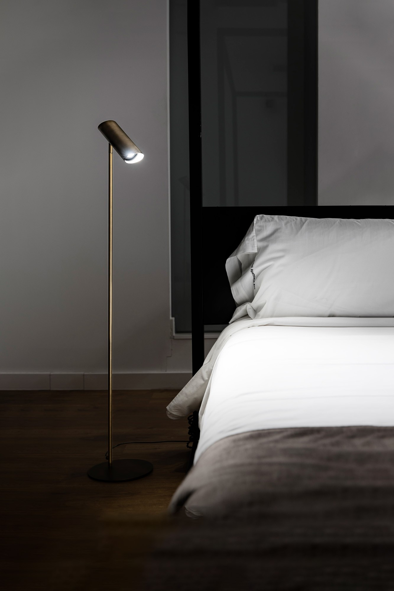 Una lampada da terra moderna illumina un letto bianco con coperta marrone.