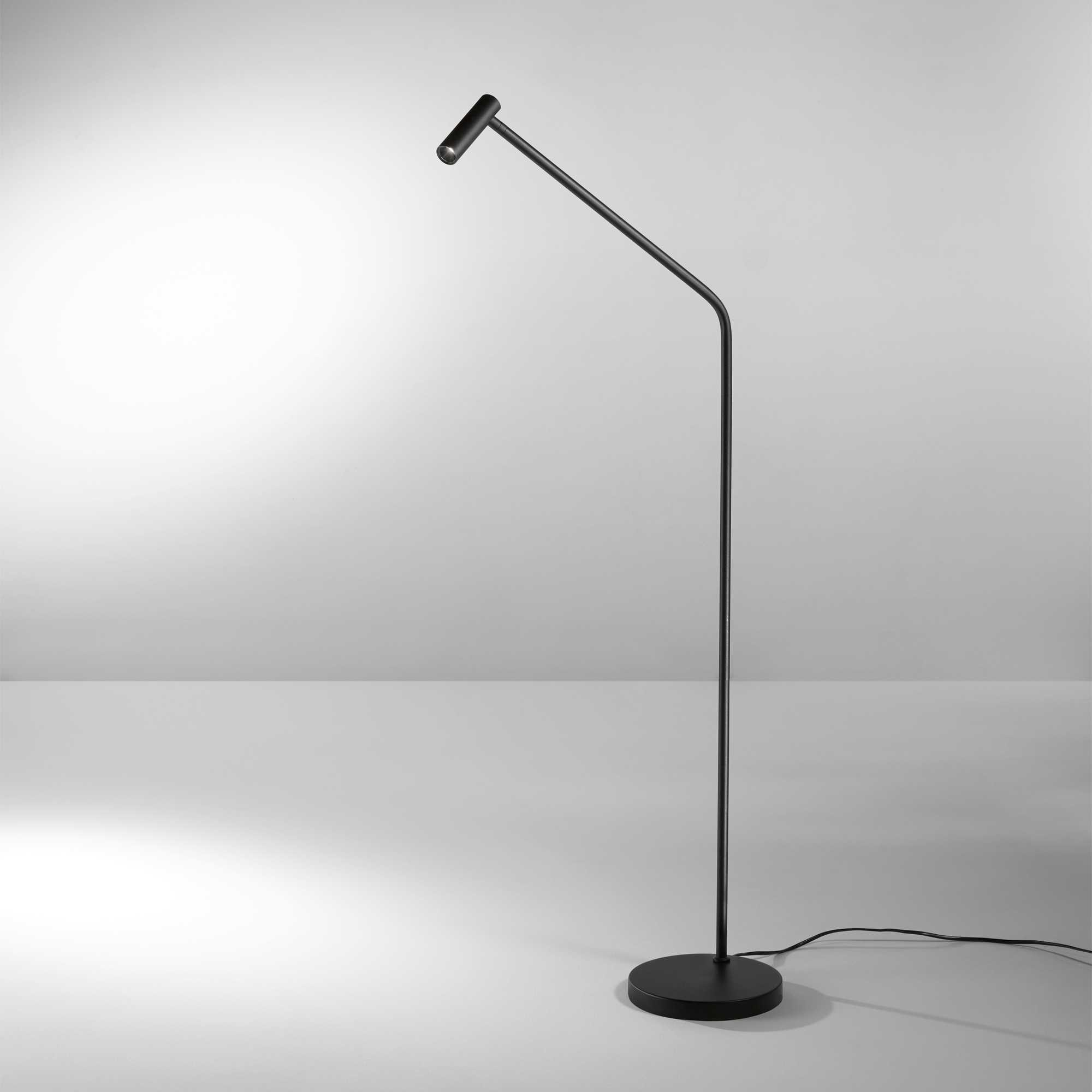 Un braccio di lampada da terra nero e snello si estende da una base rotonda. La luce brilla.