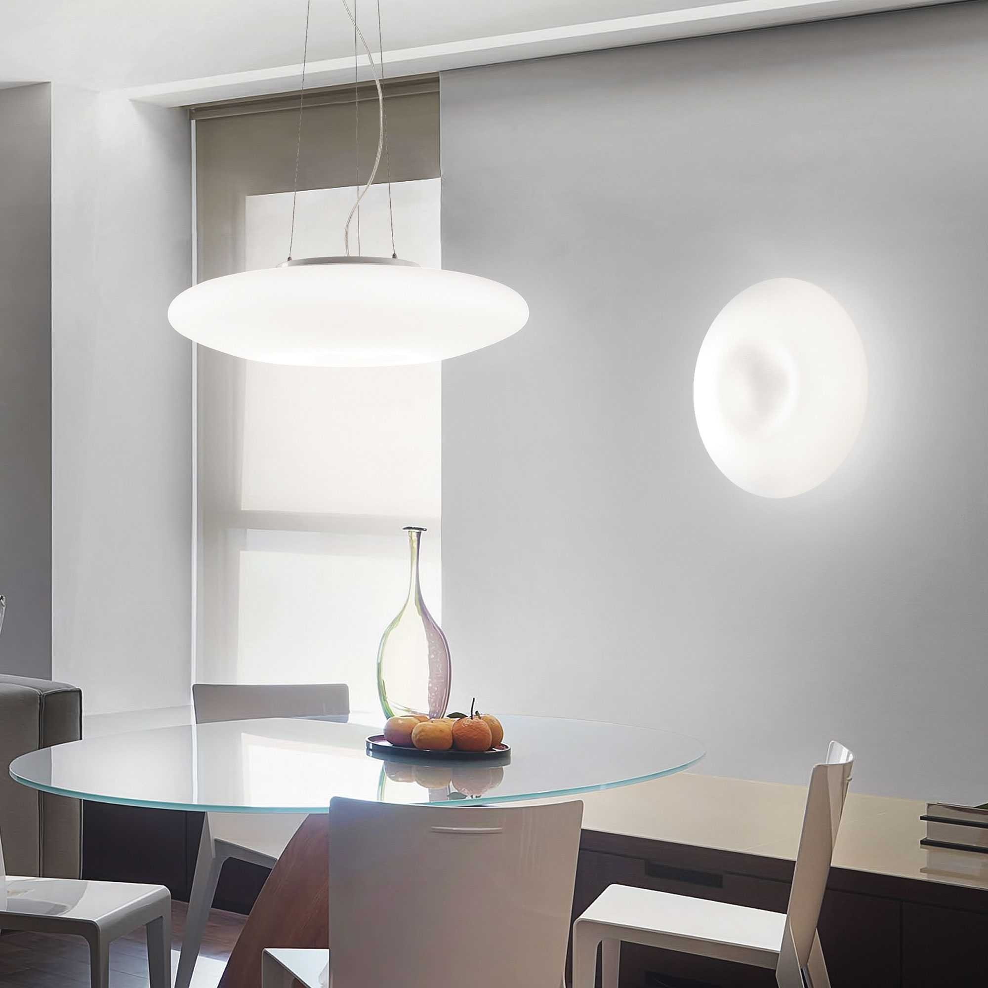 Un tavolo da pranzo in vetro con sedie bianche, illuminato da una lampada a sospensione.