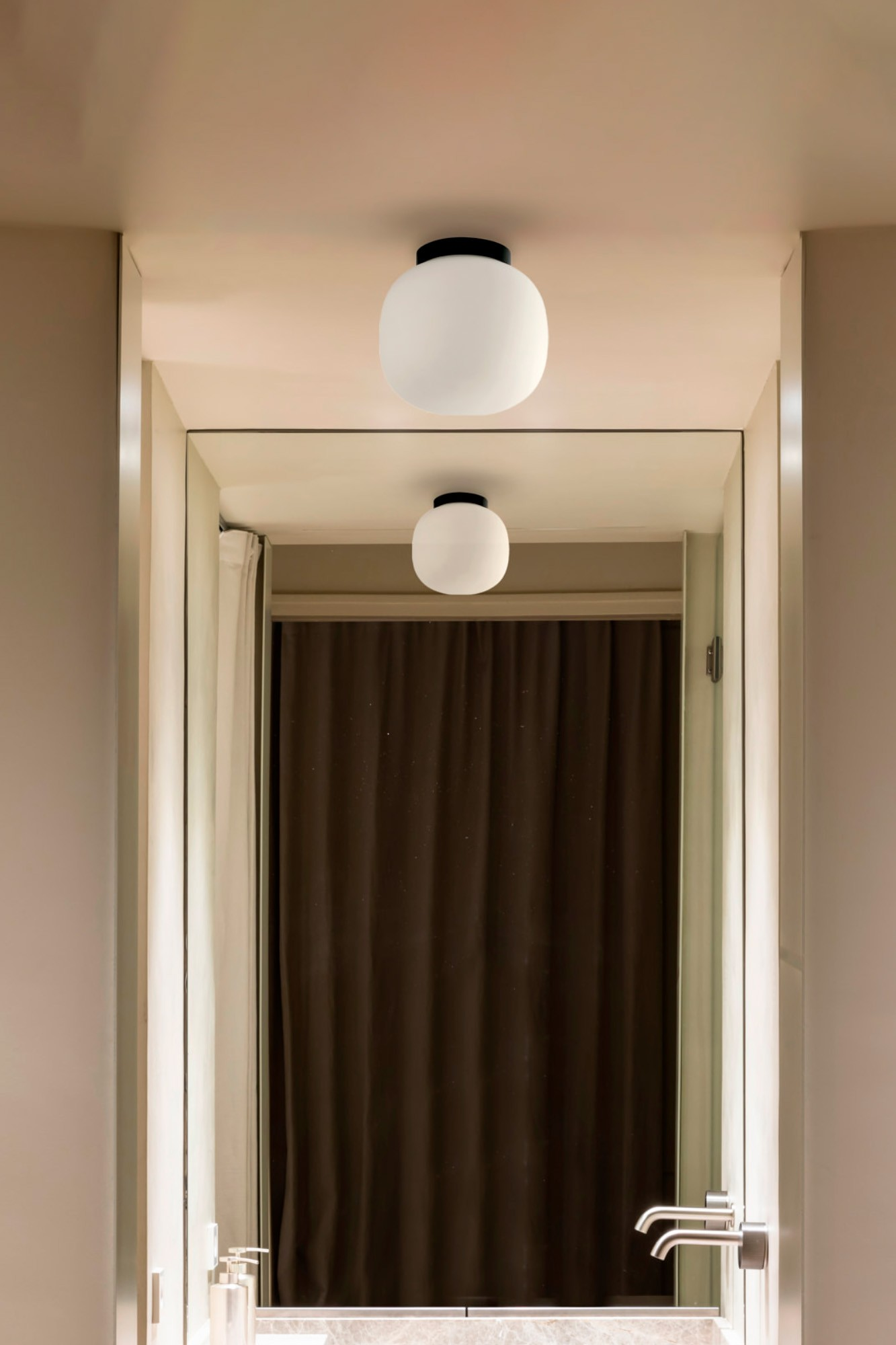 Specchio mostra lampada, tenda e rubinetti in un bagno.