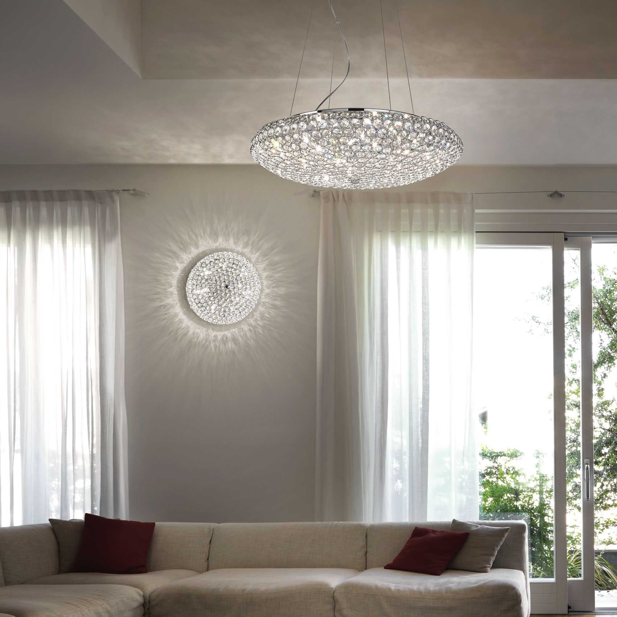 Un lampadario rotondo di cristallo appeso sopra un divano angolare con cuscini rossi.
