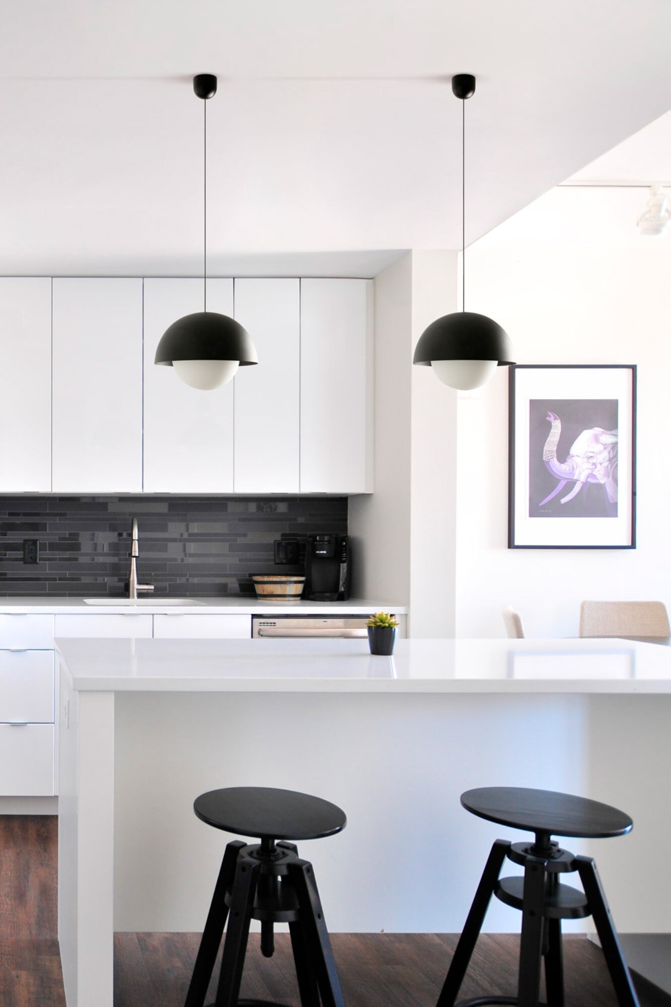 Cucina moderna con bancone bianco, sgabelli da bar e quadro d'elefante.