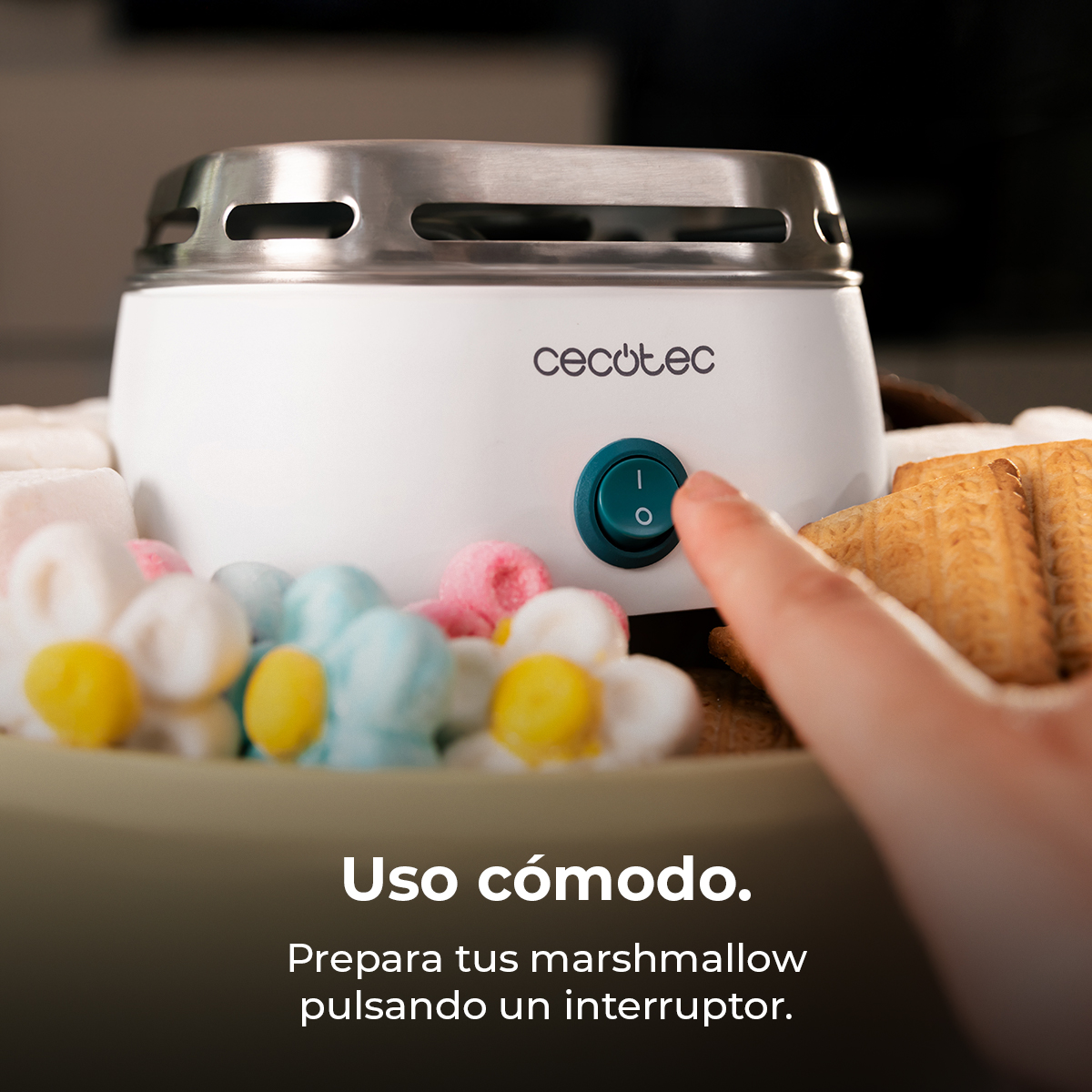 Un dito preme un pulsante verde su una tostiera per marshmallow bianca con marshmallow colorati.