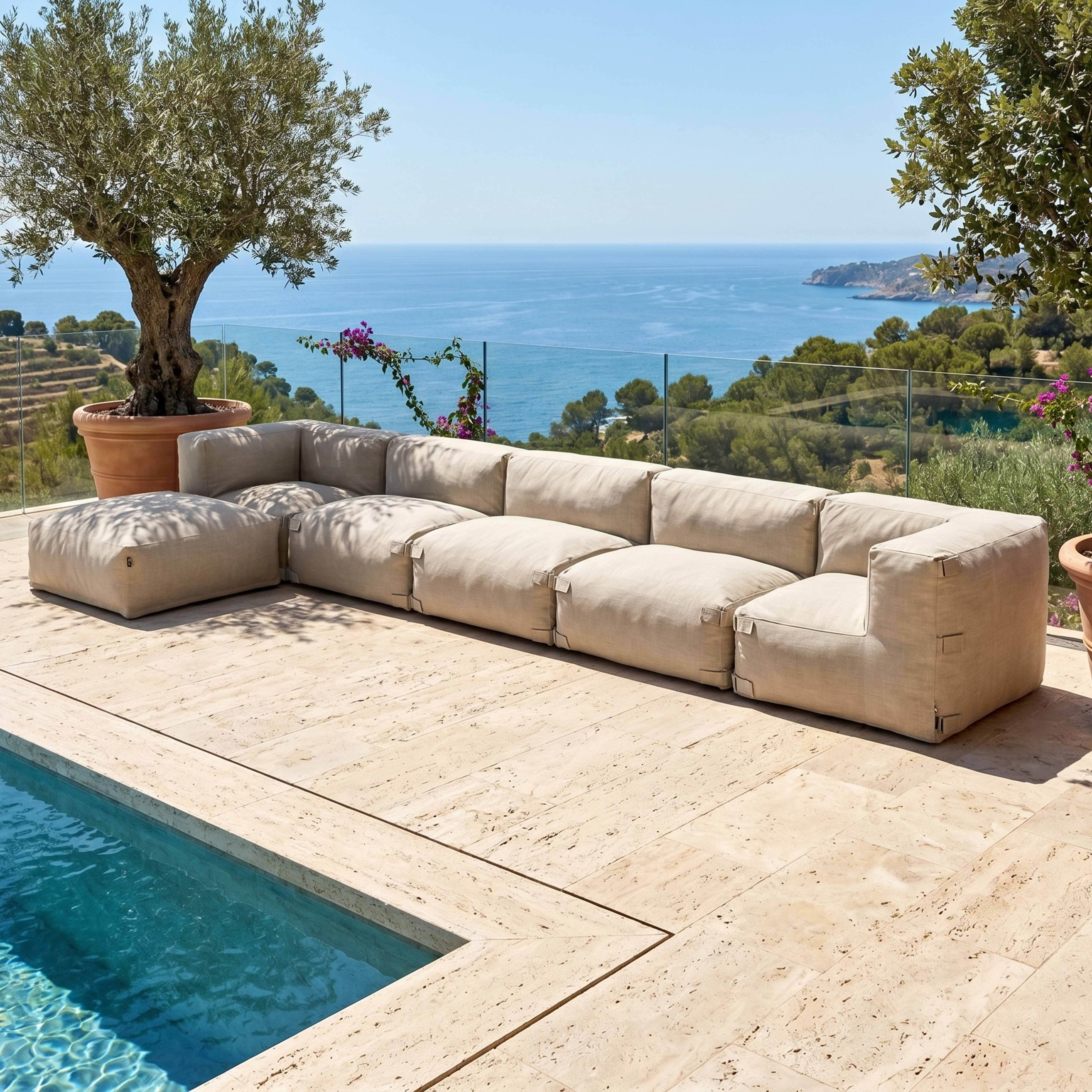 Eine beigefarbene modulare Couch steht auf einer Steinterrasse neben einem Pool mit Blick auf das Meer.