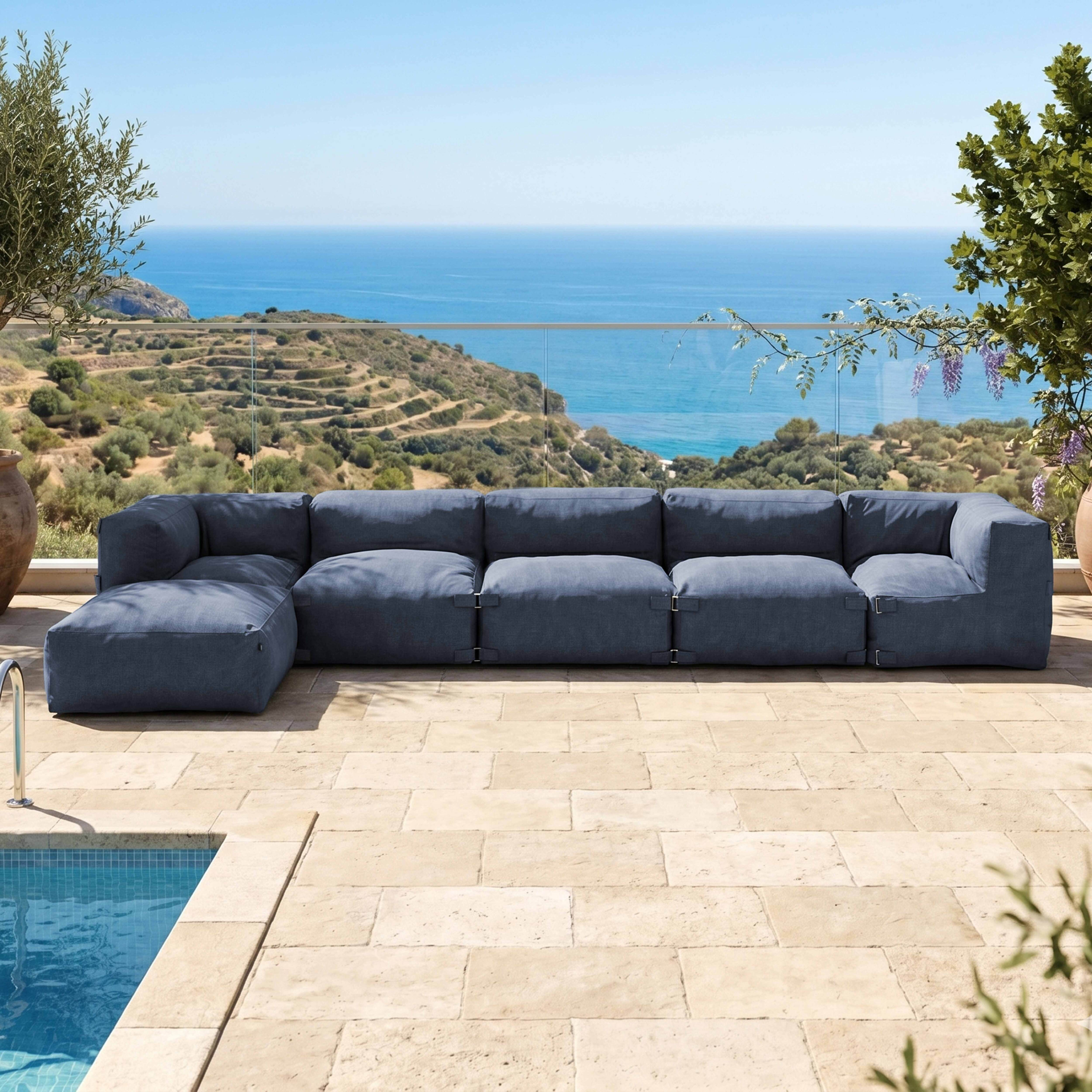 Ein großes, blaues Modulsofa steht auf einer Steinterrasse mit Blick auf das Meer.