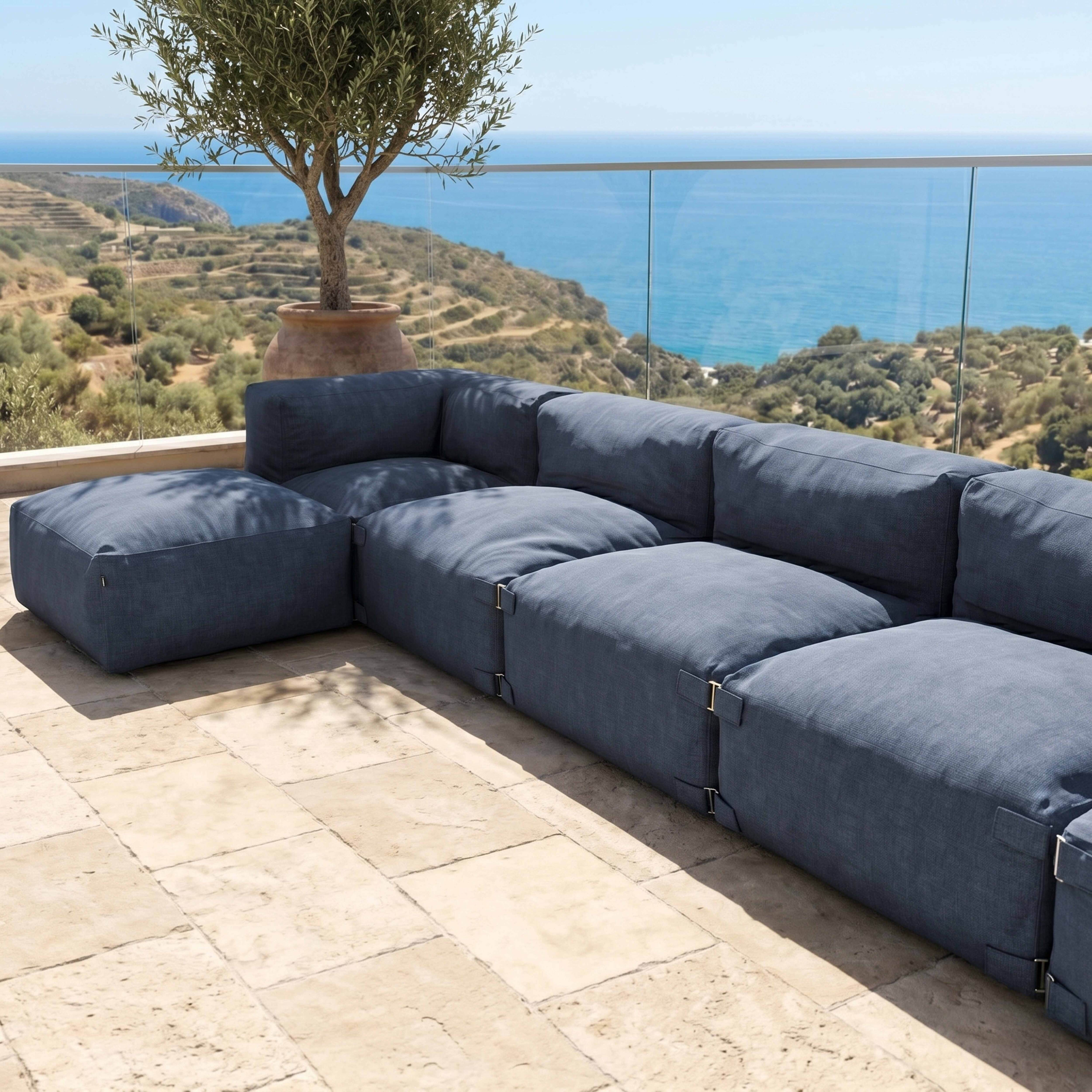 Ein dunkles, modulares Sofa steht auf einer Steinterrasse mit Blick auf das Meer.
