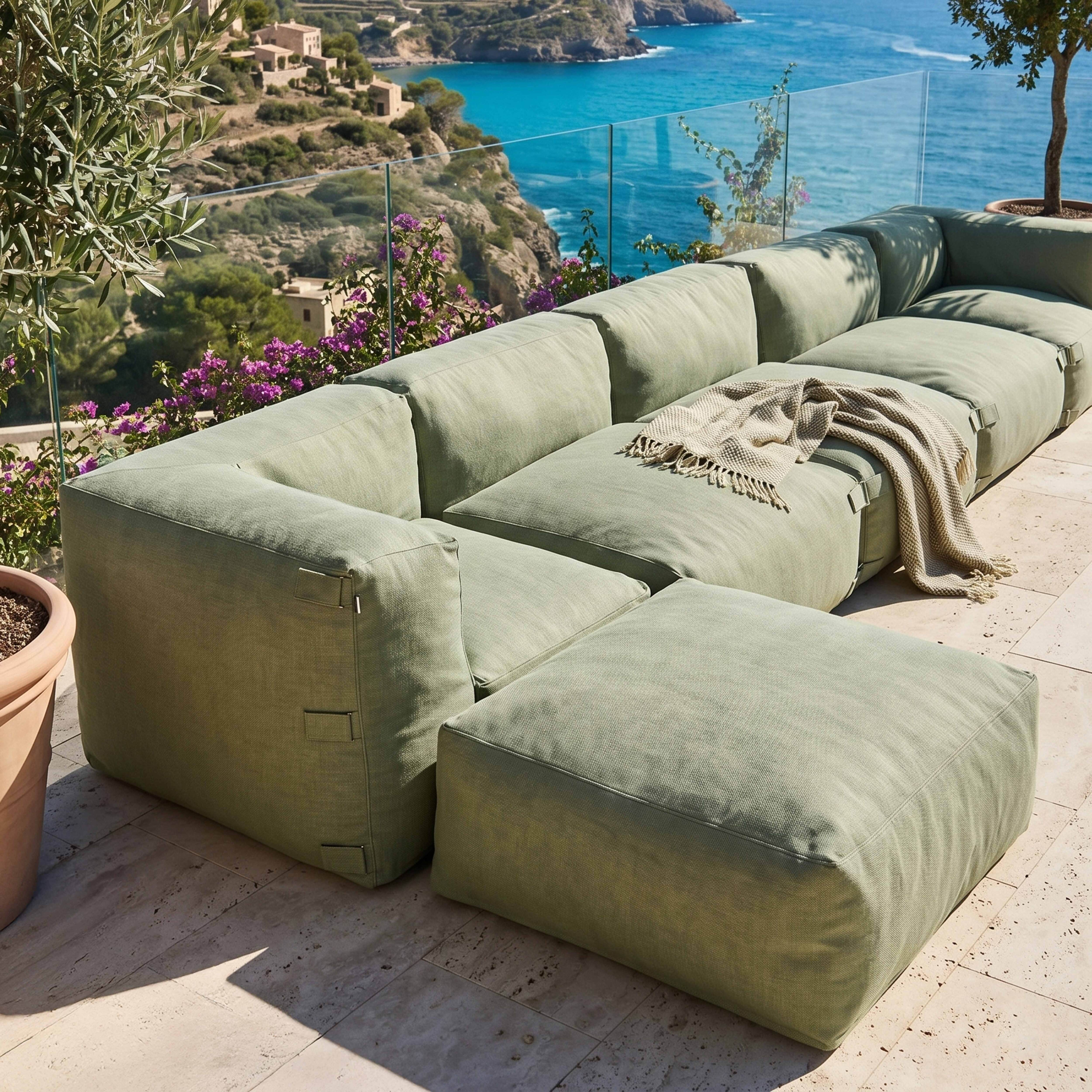 Ein modulares grünes Sofa mit einer Decke auf einer gefliesten Terrasse mit Meerblick.