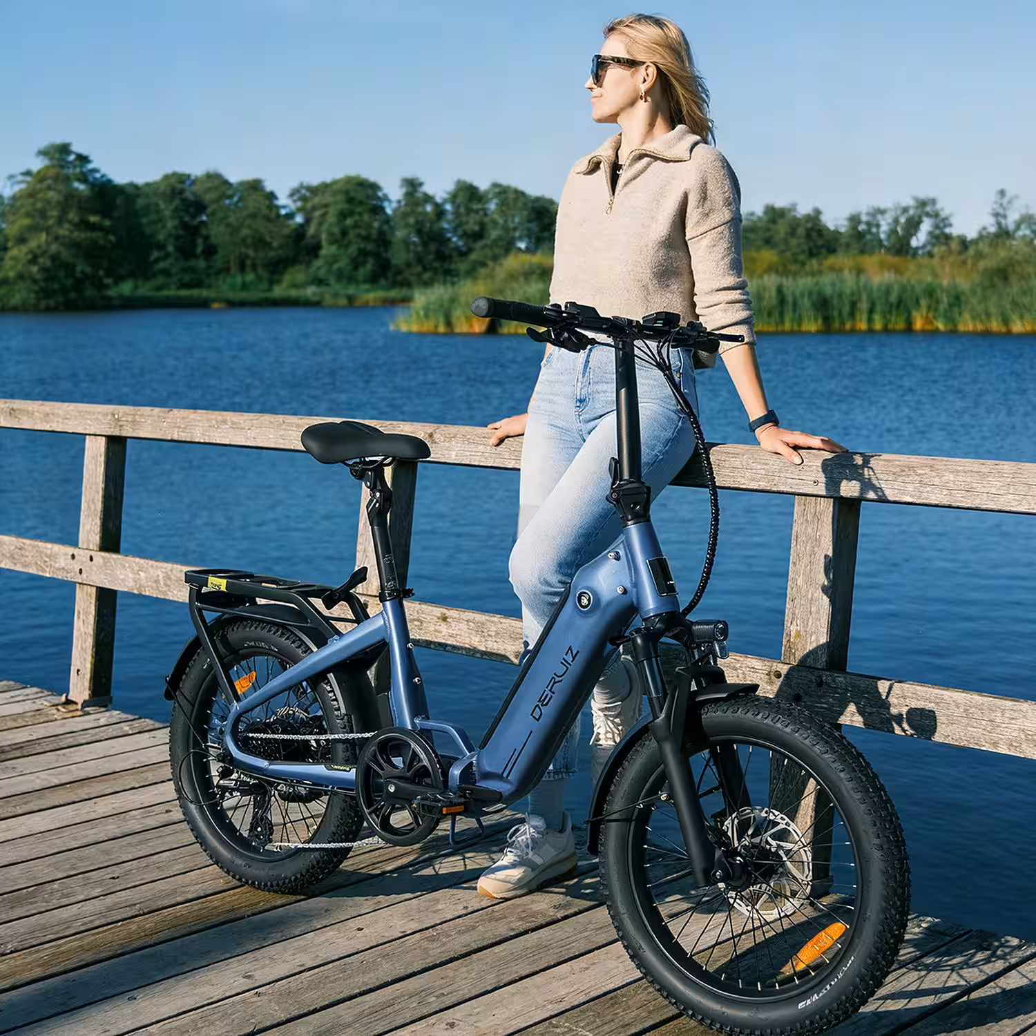 Frau mit blauem E-Bike auf Holzsteg am See, Bäume im Hintergrund.