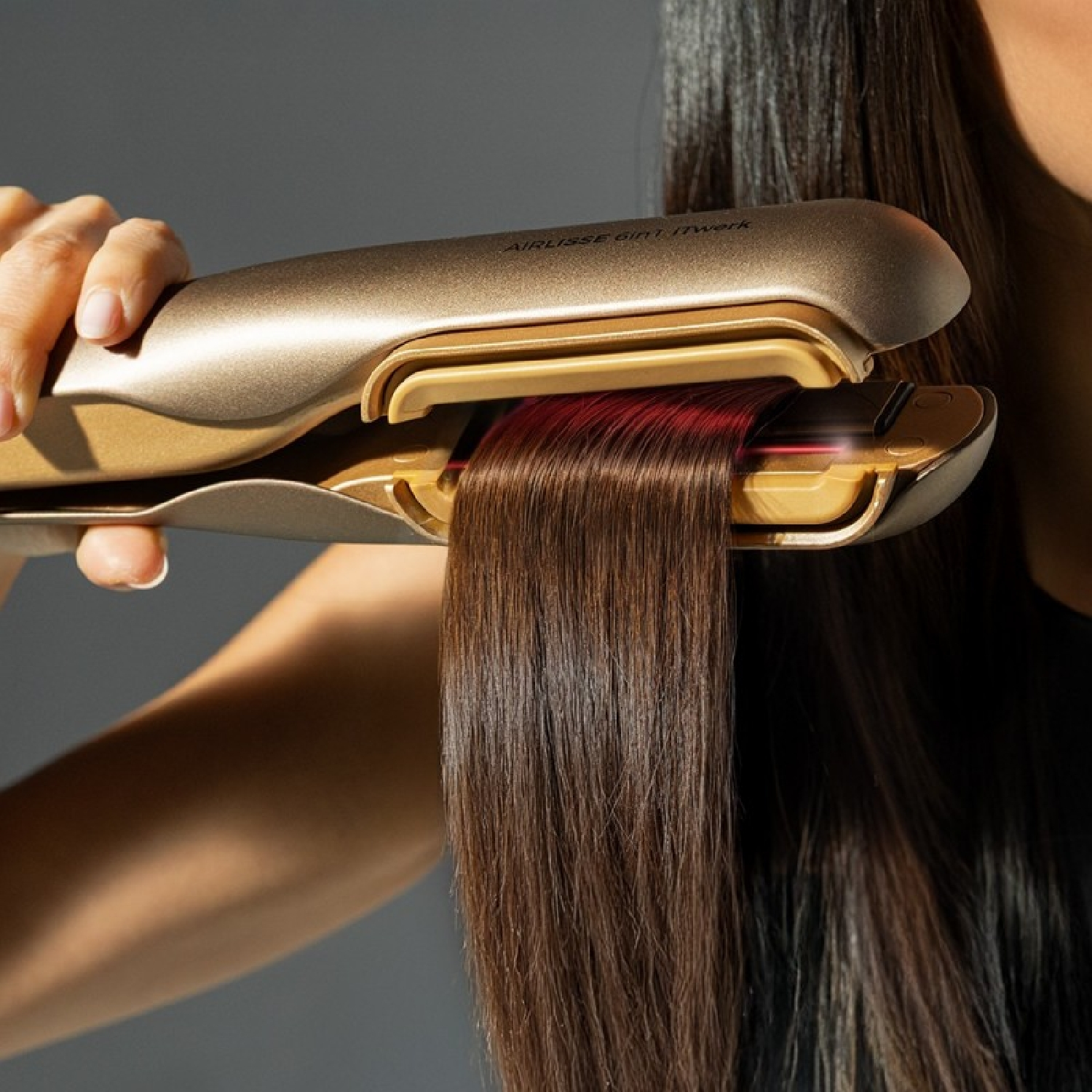 Una mano sujeta una plancha dorada para el pelo, alisando pelo castaño.