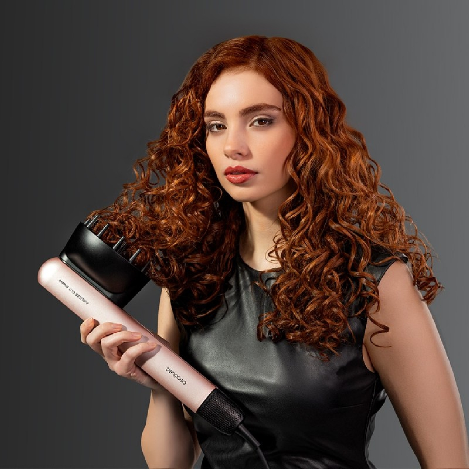 Donna con capelli rossi ricci tiene un asciugacapelli rosa con diffusore.