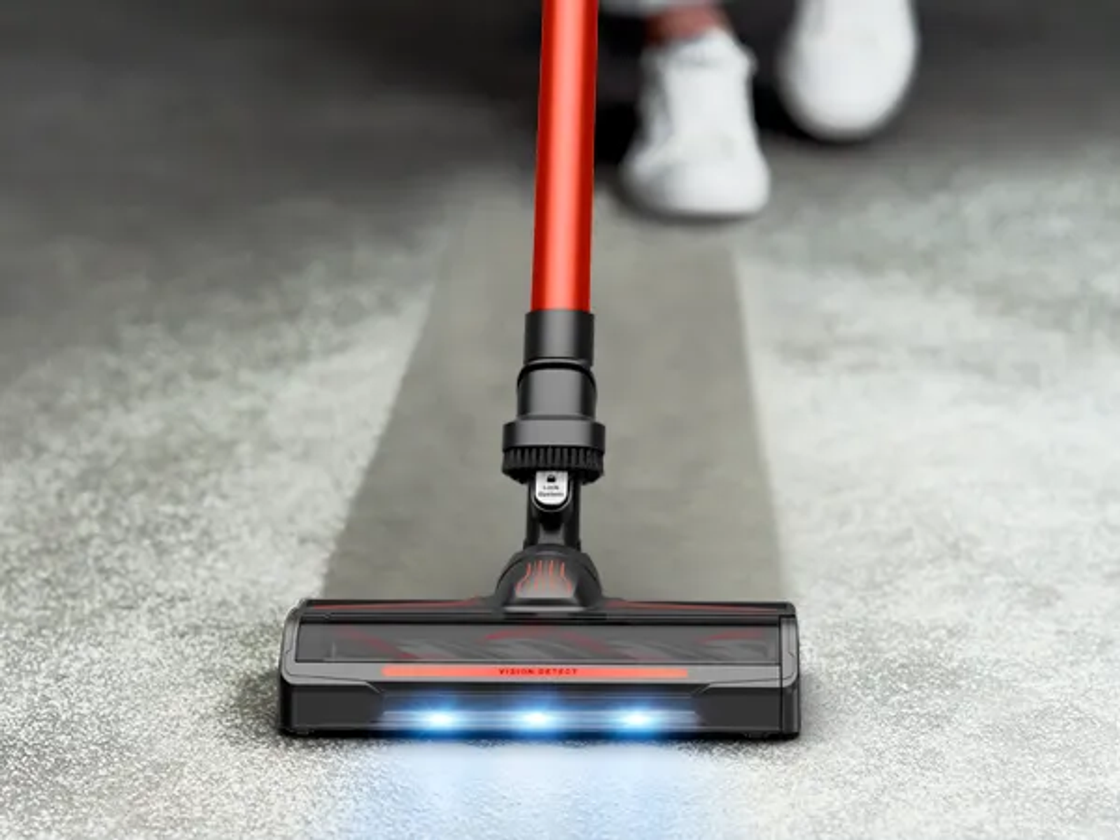 Una testina aspirapolvere rossa con luci blu pulisce un tappeto grigio.