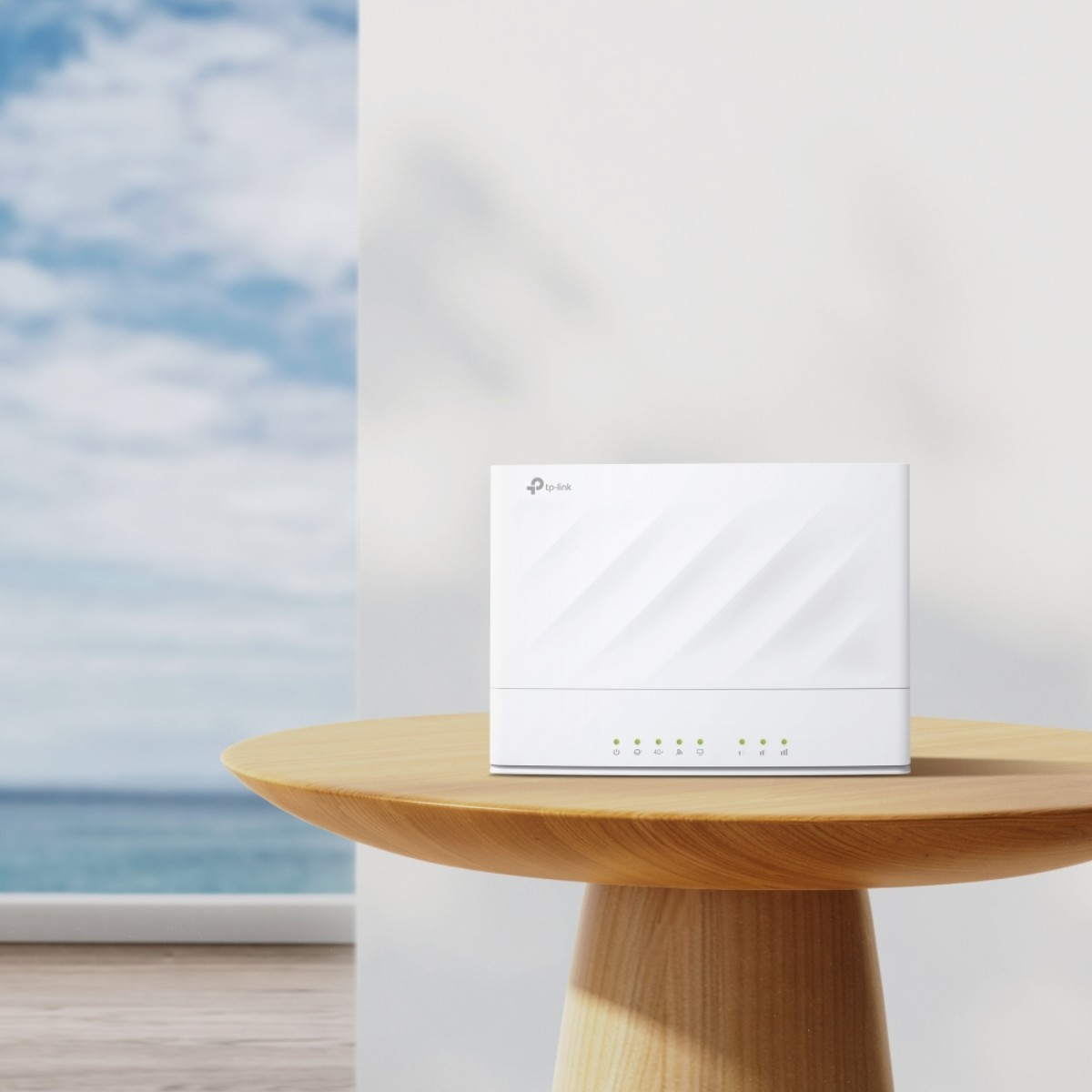 Un router TP-Link bianco su un tavolo di legno, con sfondo sfocato di oceano e cielo.