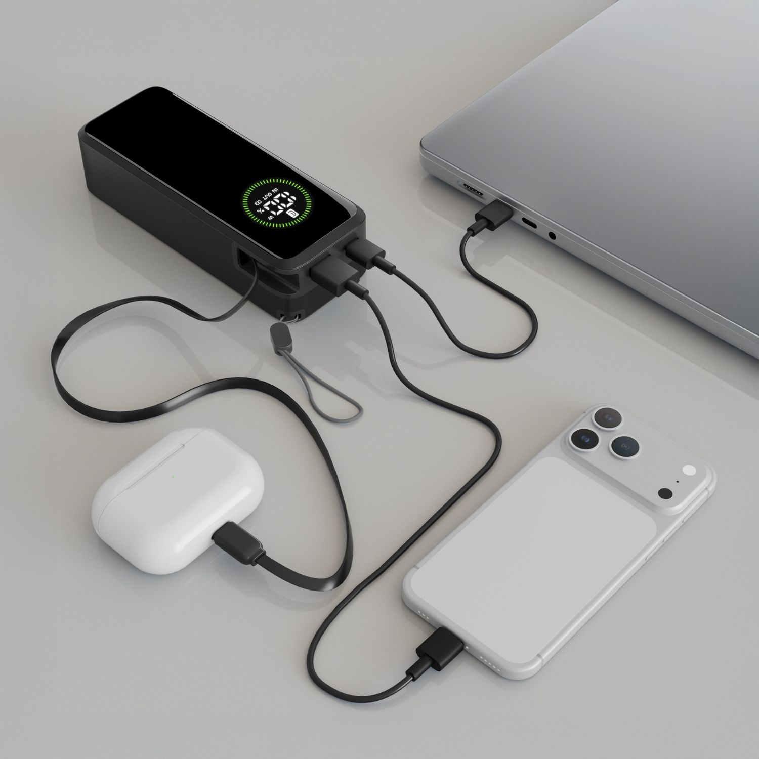 Eine schwarze Powerbank lädt einen Laptop, ein Telefon und eine Kopfhörerhülle.