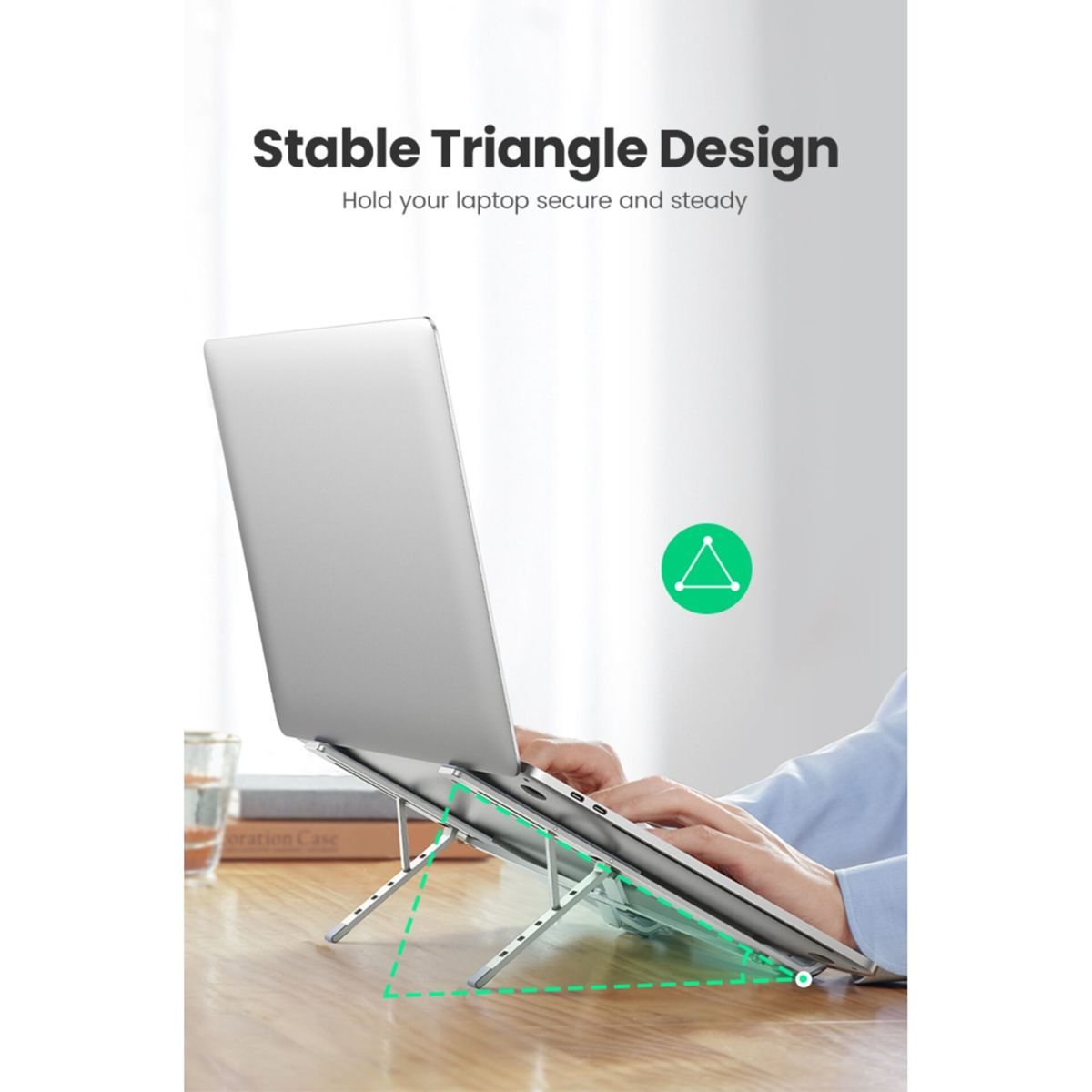 Ein Laptop steht auf einem silbernen Ständer mit Dreiecksdesign. Hände tippen auf der Tastatur.