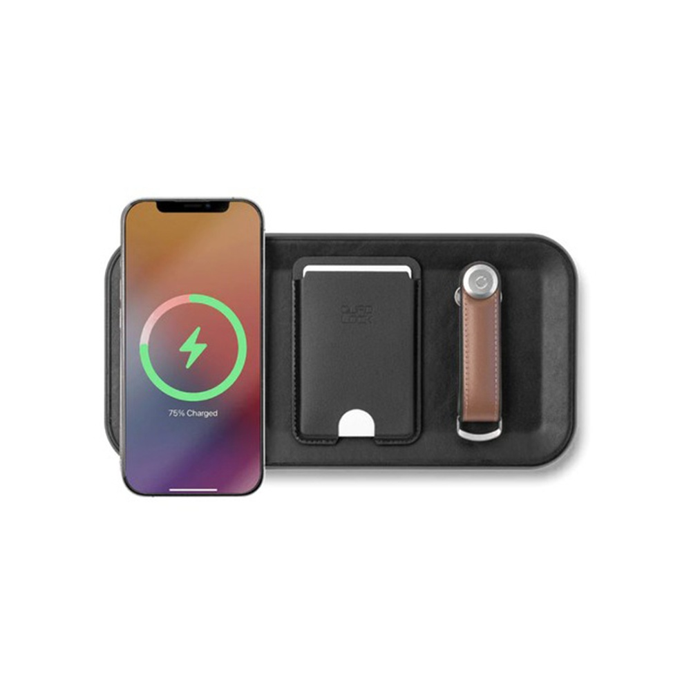 iPhone ładuje się na czarnej stacji ładującej, obok karty i breloczka na klucze.