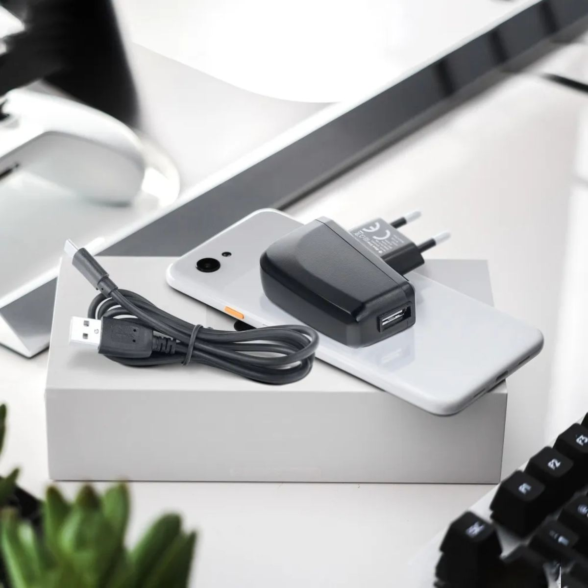 Un smartphone blanco con cargador negro y cable USB sobre una caja blanca.