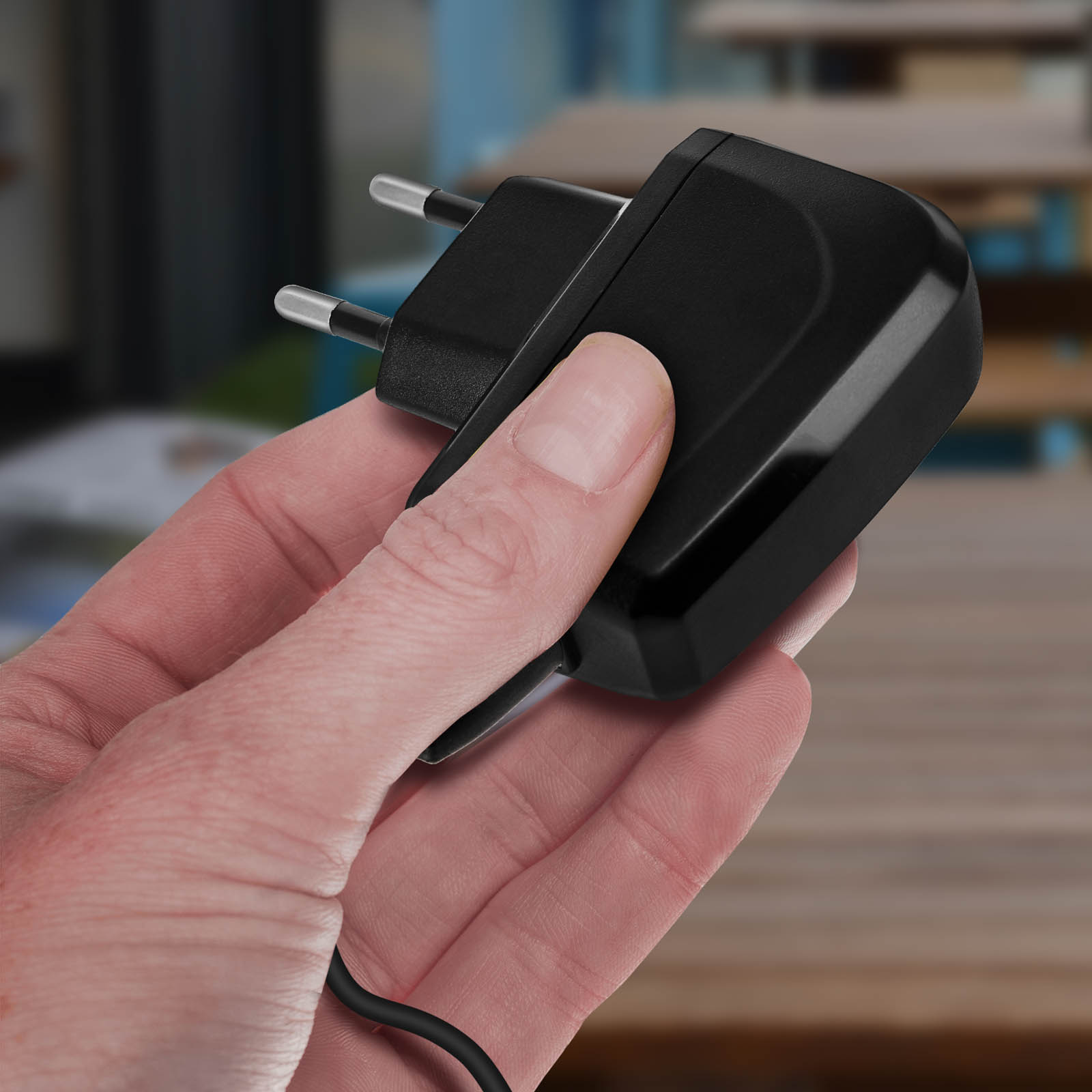 Una mano sostiene un adaptador de corriente negro con dos clavijas metálicas.