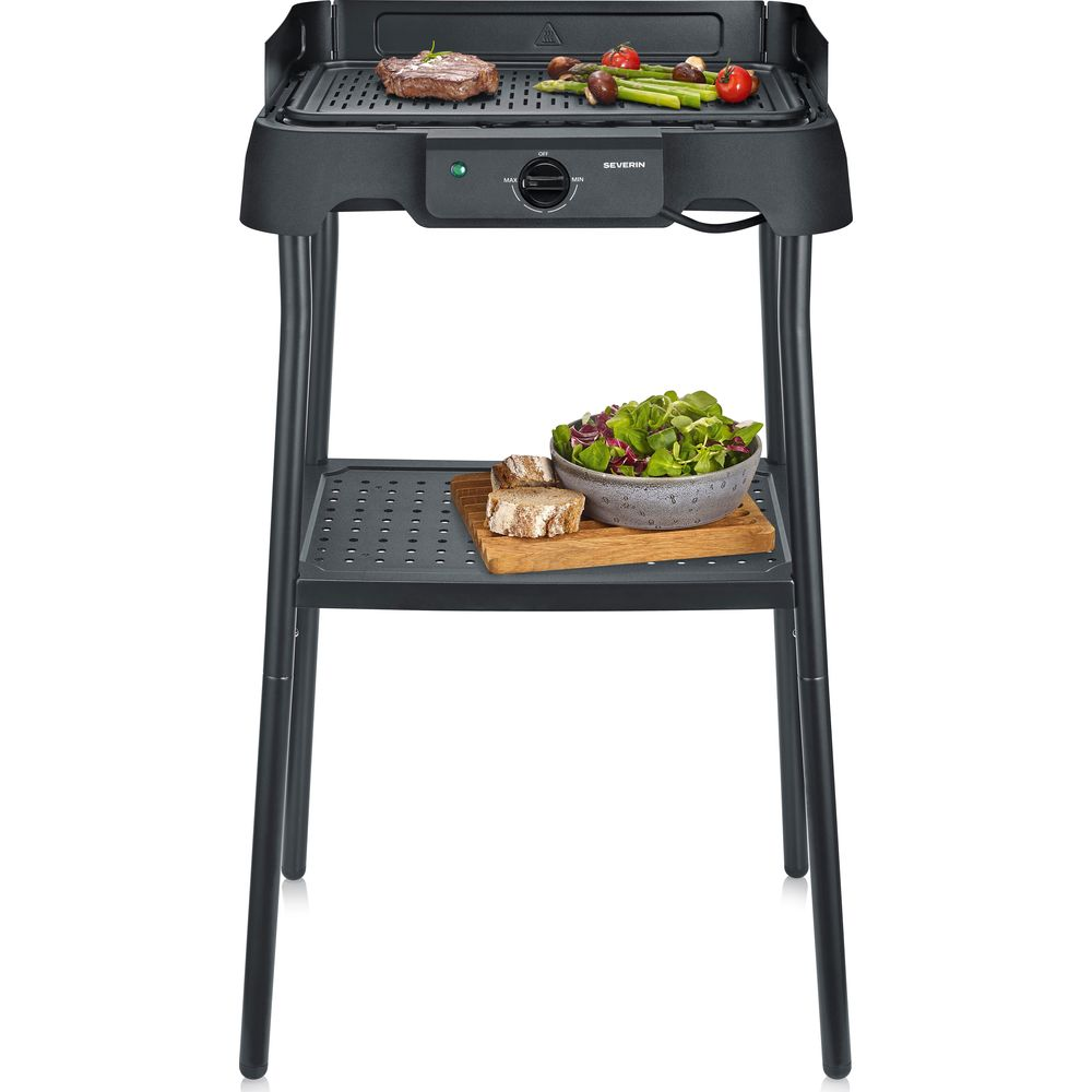 Una parrilla eléctrica negra con carne y verduras en la rejilla y ensalada en el estante.