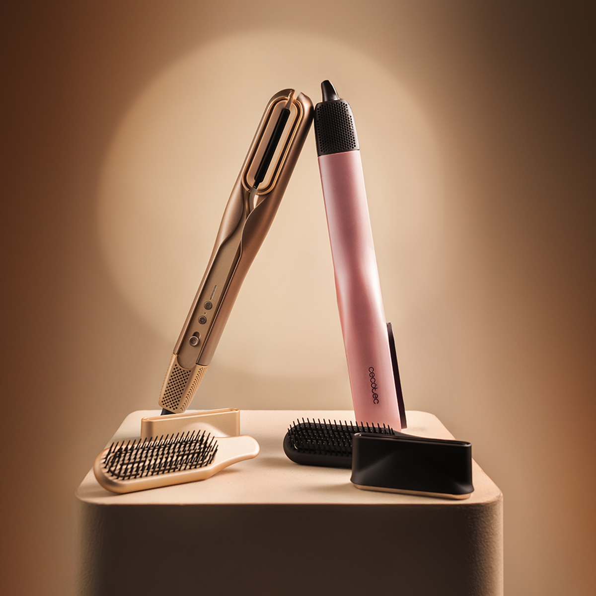 Due piastre per capelli, una oro, una rosa, con spazzole su un piedistallo.