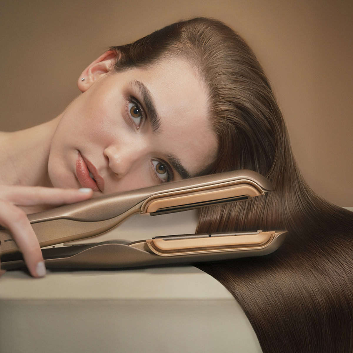 Donna con lunghi capelli castani e una piastra che le liscia i capelli.