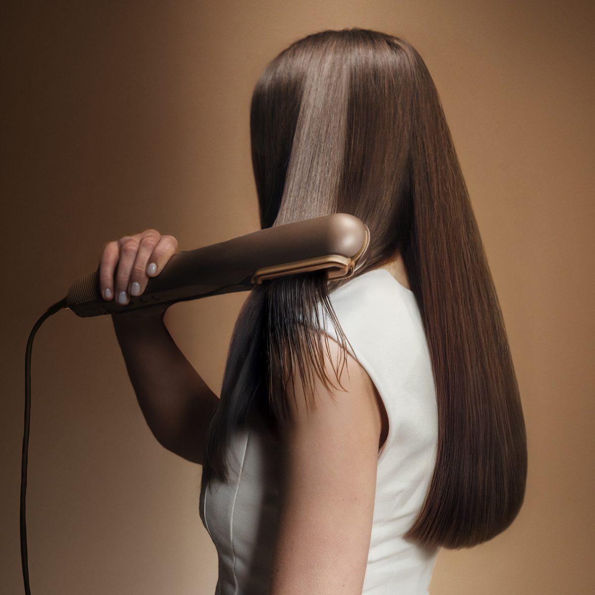 Donna piastra i capelli castani con piastra dorata su sfondo marrone.