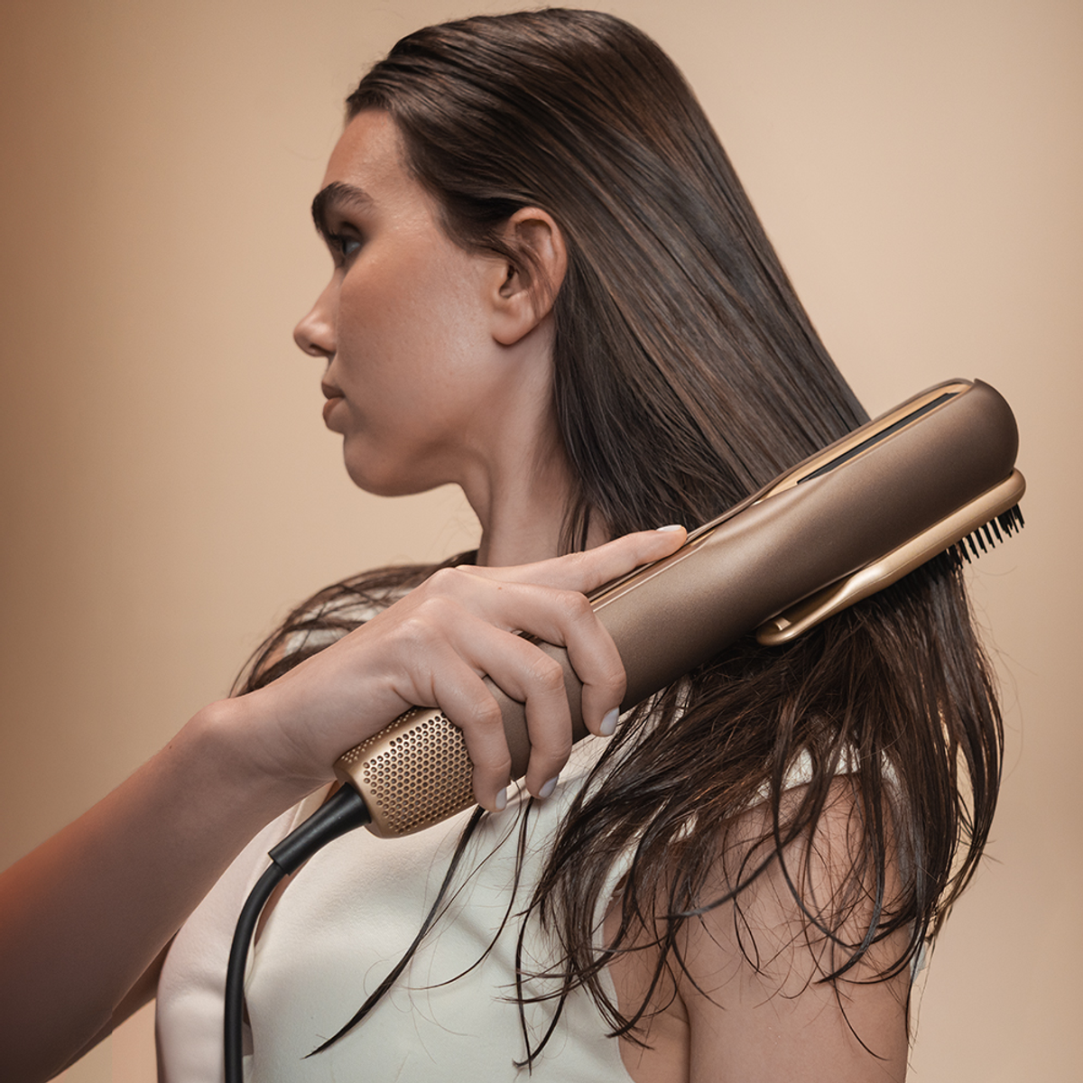 Una donna con lunghi capelli castani usa una piastra dorata.