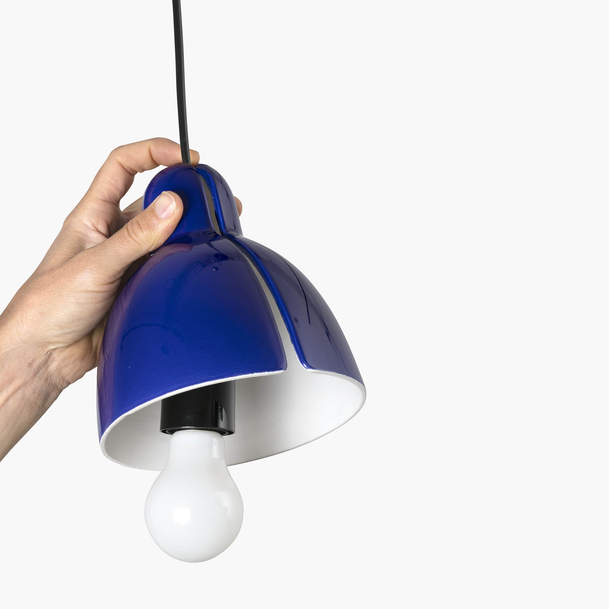 Una mano tiene un paralume blu con una lampadina bianca.