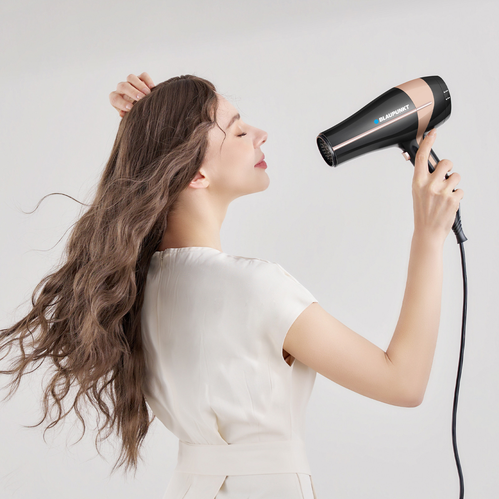 Una donna asciuga i capelli castani con un asciugacapelli nero e oro.