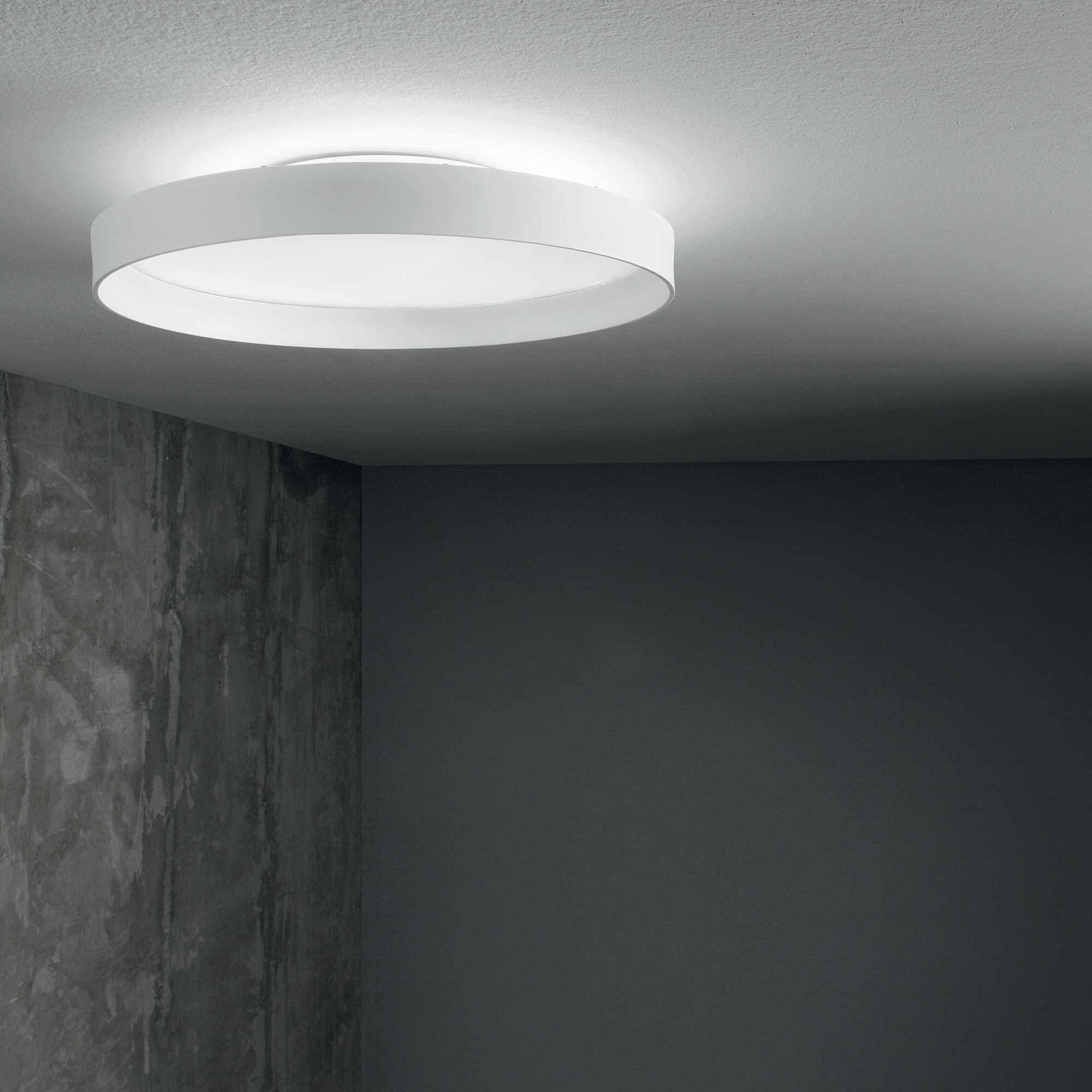 Una lampada da soffitto rotonda e bianca illumina una stanza con pareti scure.