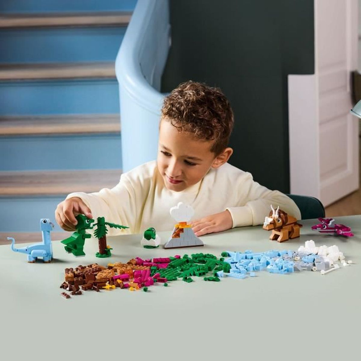 Chłopiec bawi się dinozaurami i klockami Lego na stole.