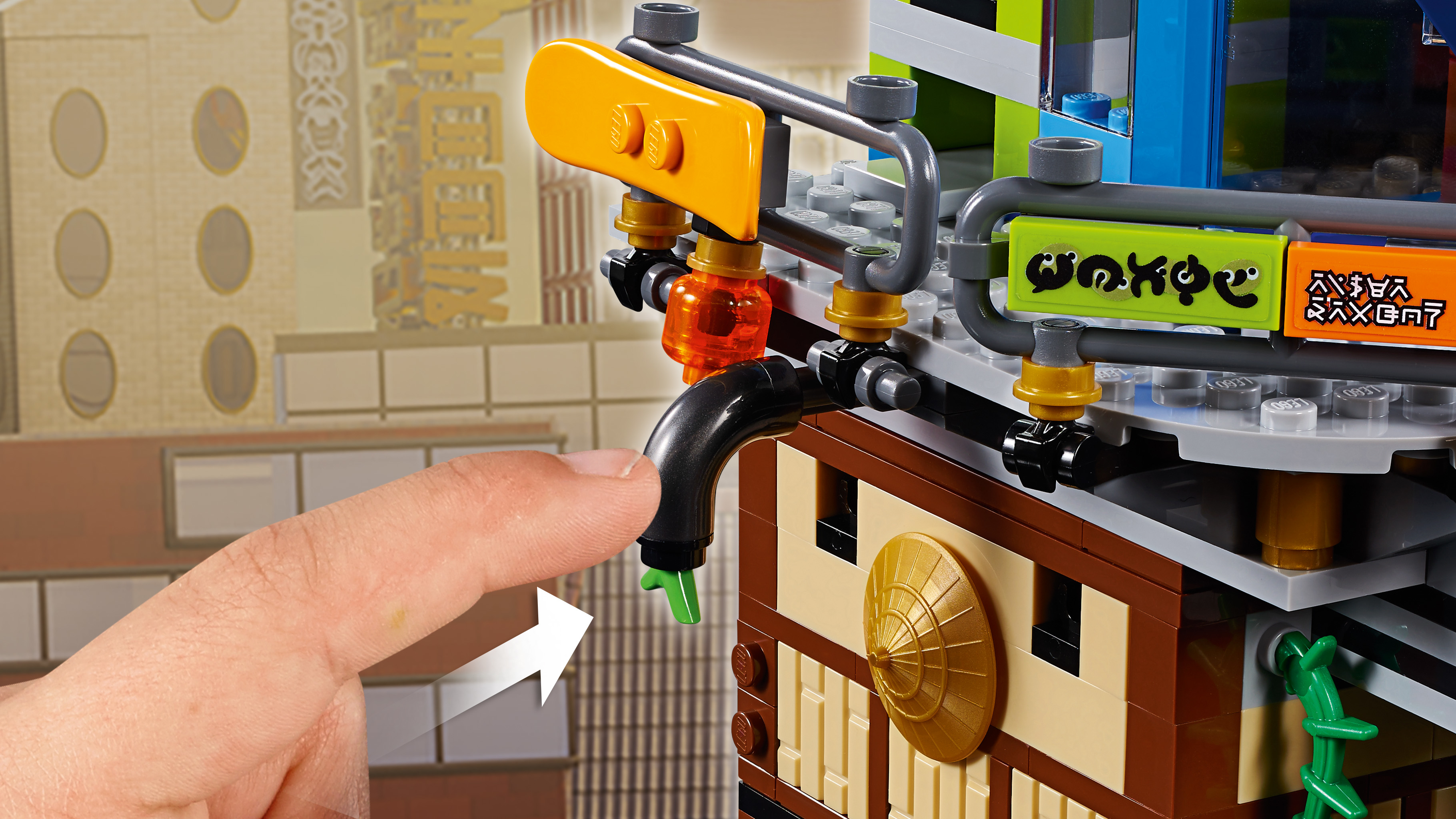 Palec naciska czarny kran na budynku Lego z żółtymi i brązowymi elementami.