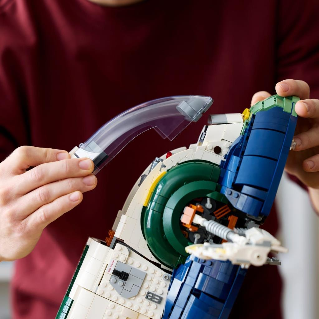 Persona che assembla un dettagliato modello di astronave con mattoncini Lego bianchi, blu e verdi.