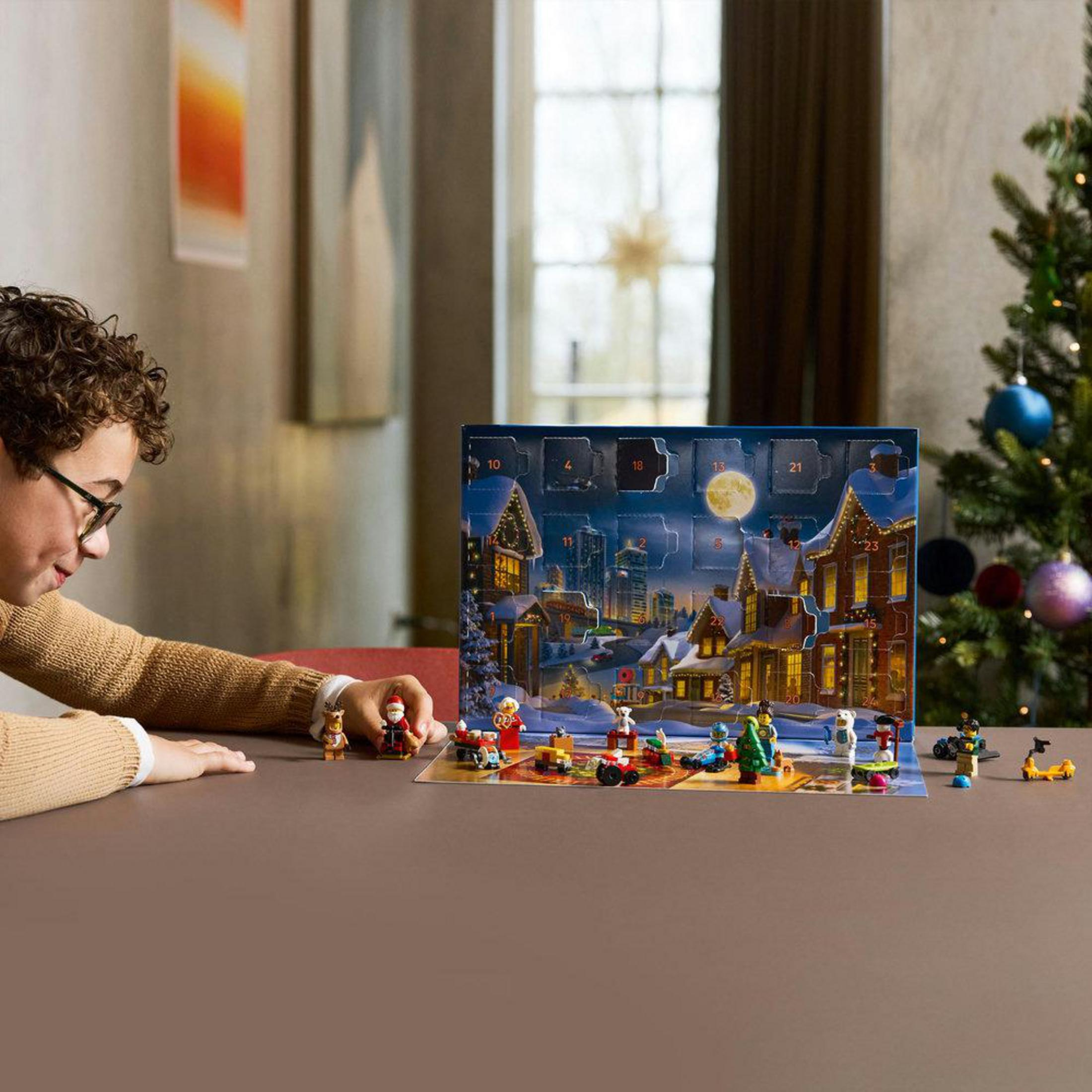 Un niño con gafas mira un calendario de adviento con figuras en miniatura y escenas navideñas.