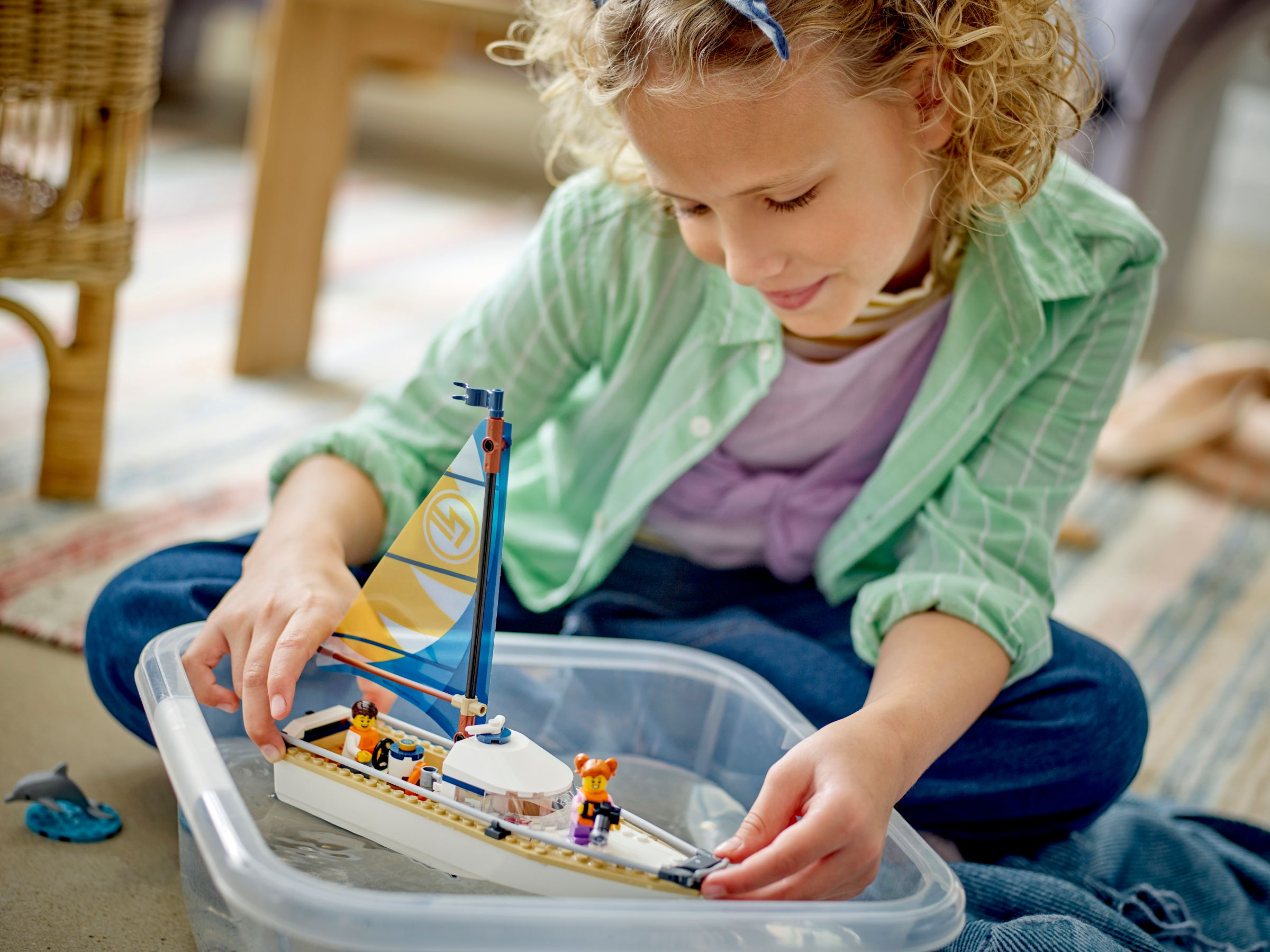 Een meisje speelt met een Lego-zeilboot in een doorzichtige bak water, met een dolfijn speelgoed.