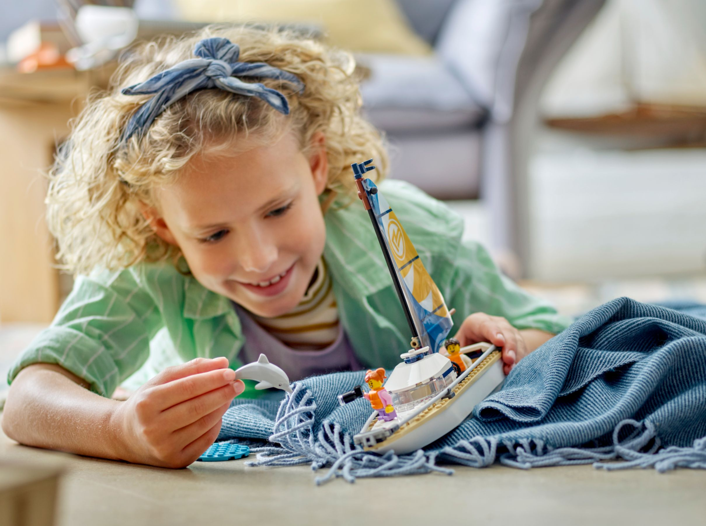 Een meisje met blond haar speelt met een Lego-zeilboot en een dolfijn.