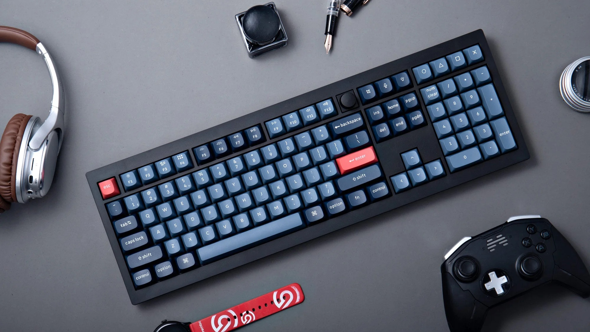 Schwarze Tastatur mit blauen Tasten, Kopfhörer, Controller und Stift auf grauem Grund.