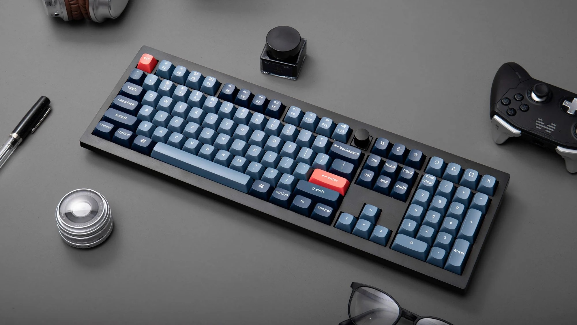 Eine Tastatur mit blauen Tasten, Esc und Enter in Rot, daneben Stifte, Kopfhörer, Controller.
