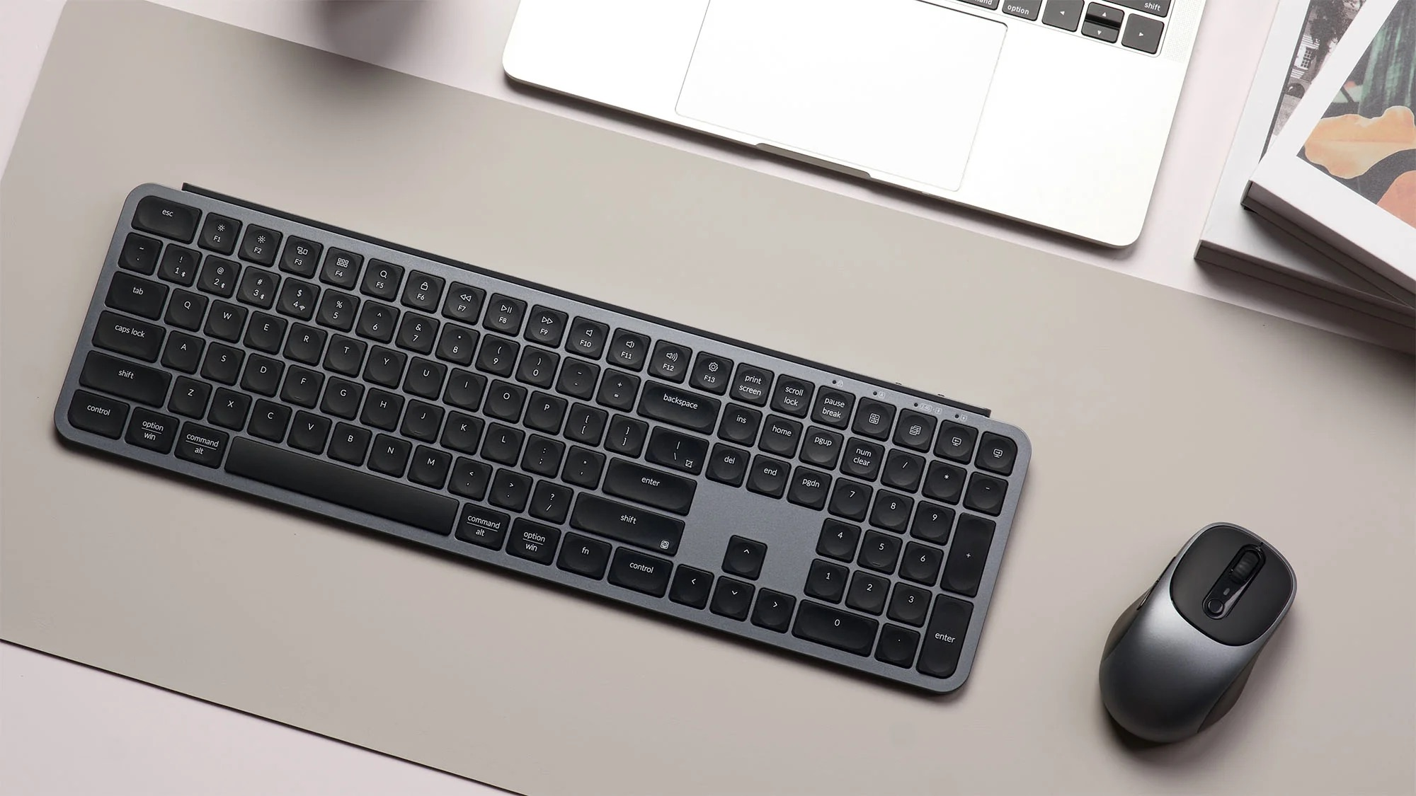 Szara klawiatura i mysz obok laptopa na jasnoszarej macie.