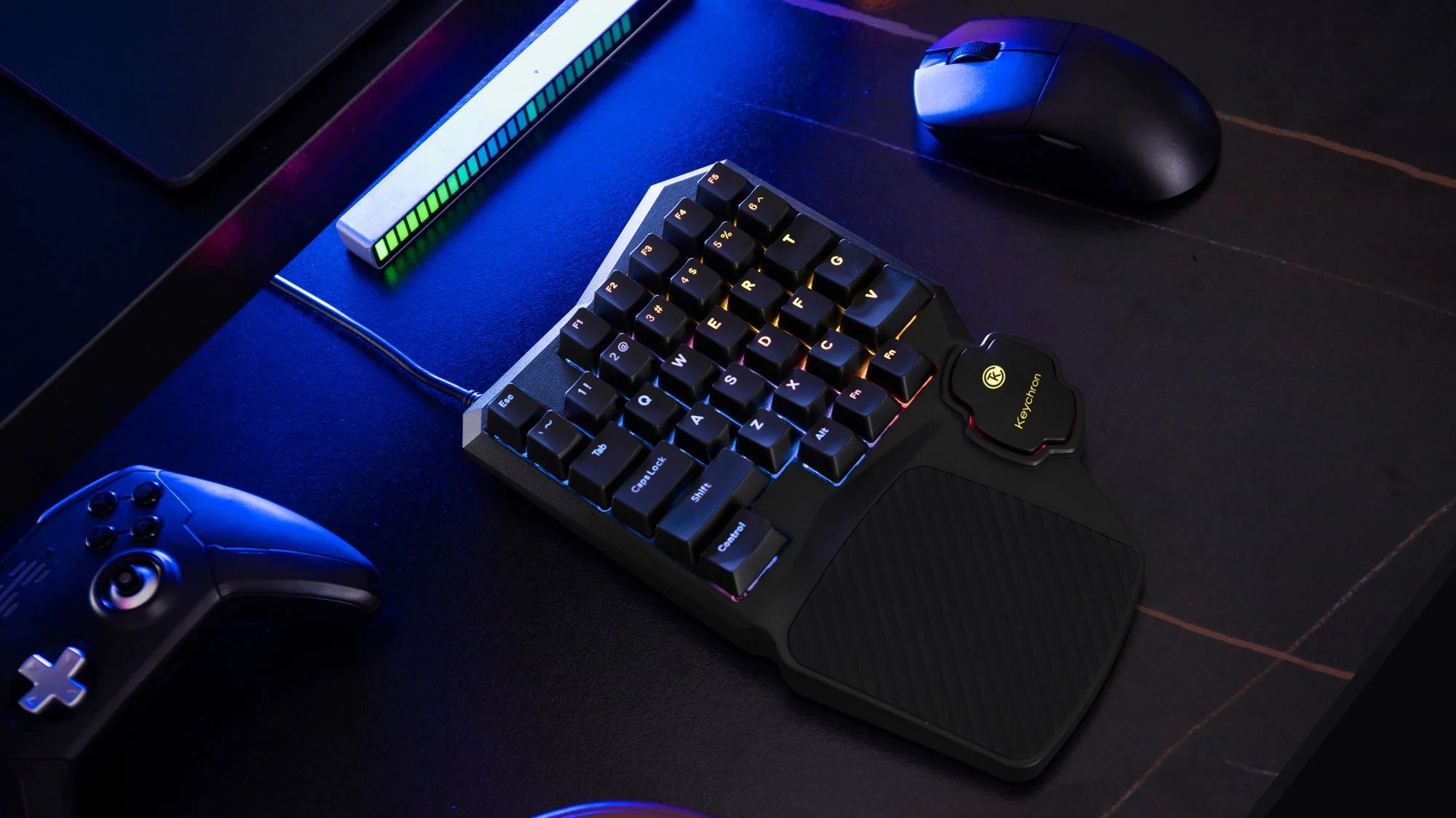 Czarna klawiatura gamingowa, mysz i kontroler na ciemnym biurku z oświetleniem RGB.